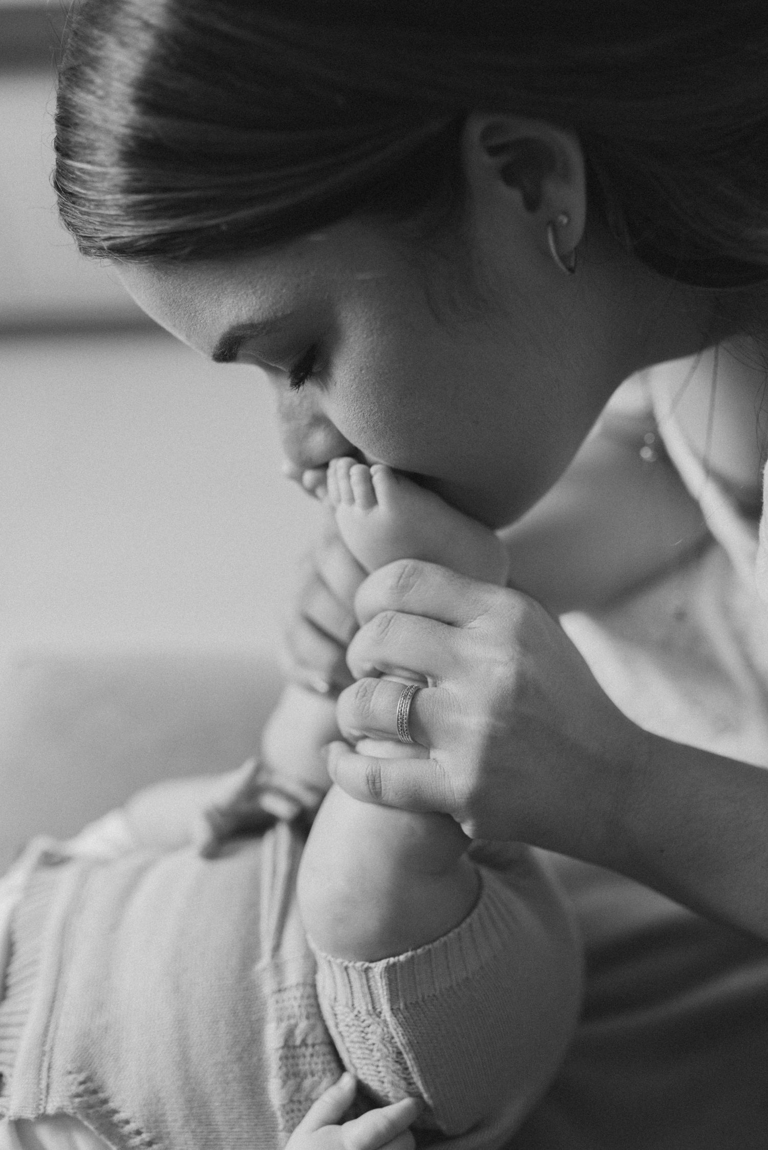 Black and white image of tender moment with baby's foot being kissed.