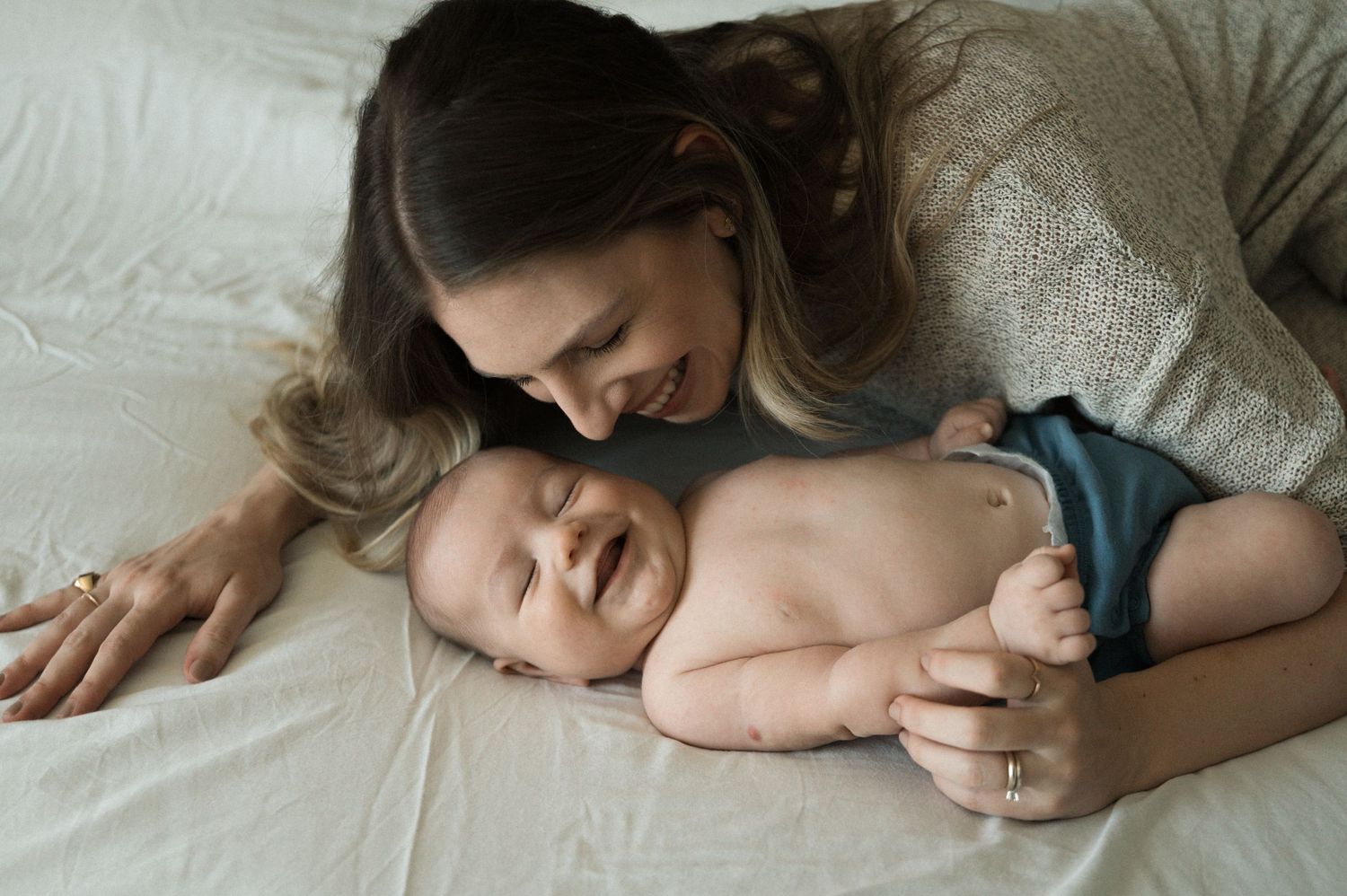 Candid lifestyle photographs showing sweet moments of connection between parents and their infant on a bed.