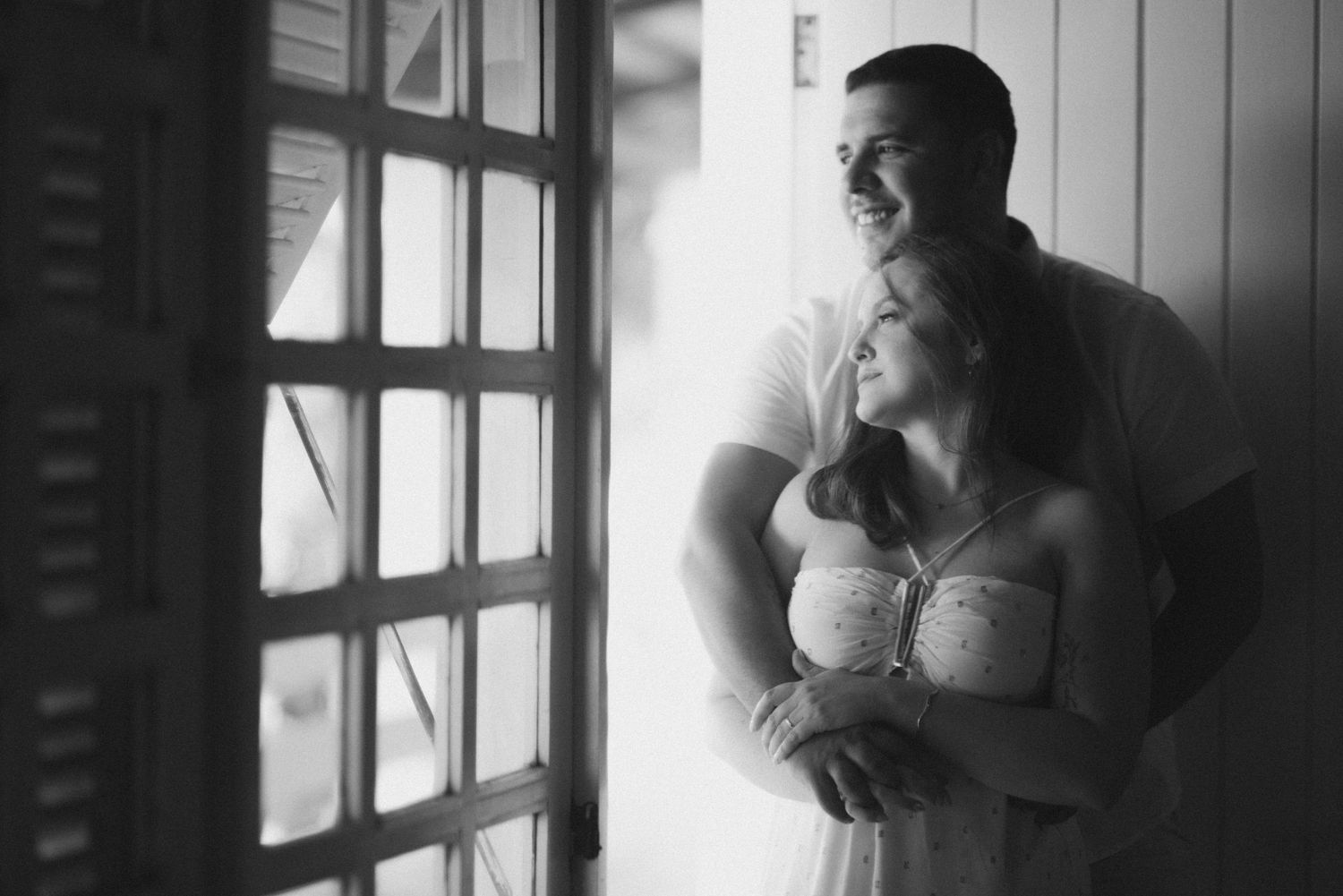 A couple share a tender moment by a window in soft monochrome light.