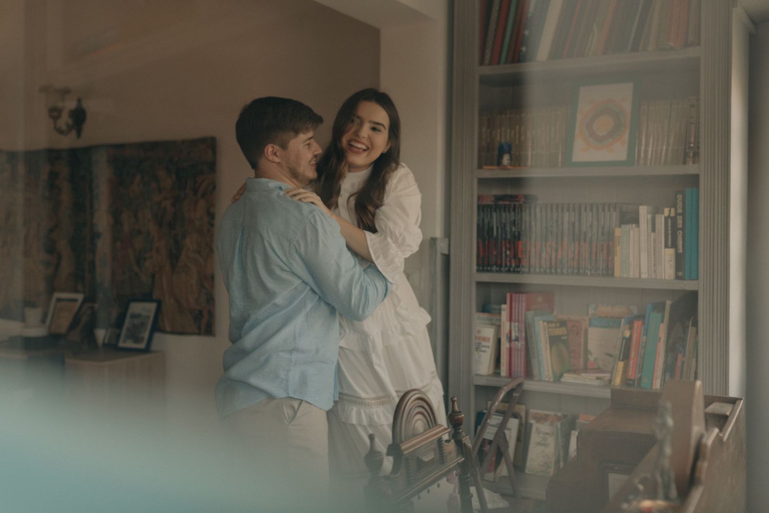 Couple sharing intimate moment in cozy room with bookshelf background.