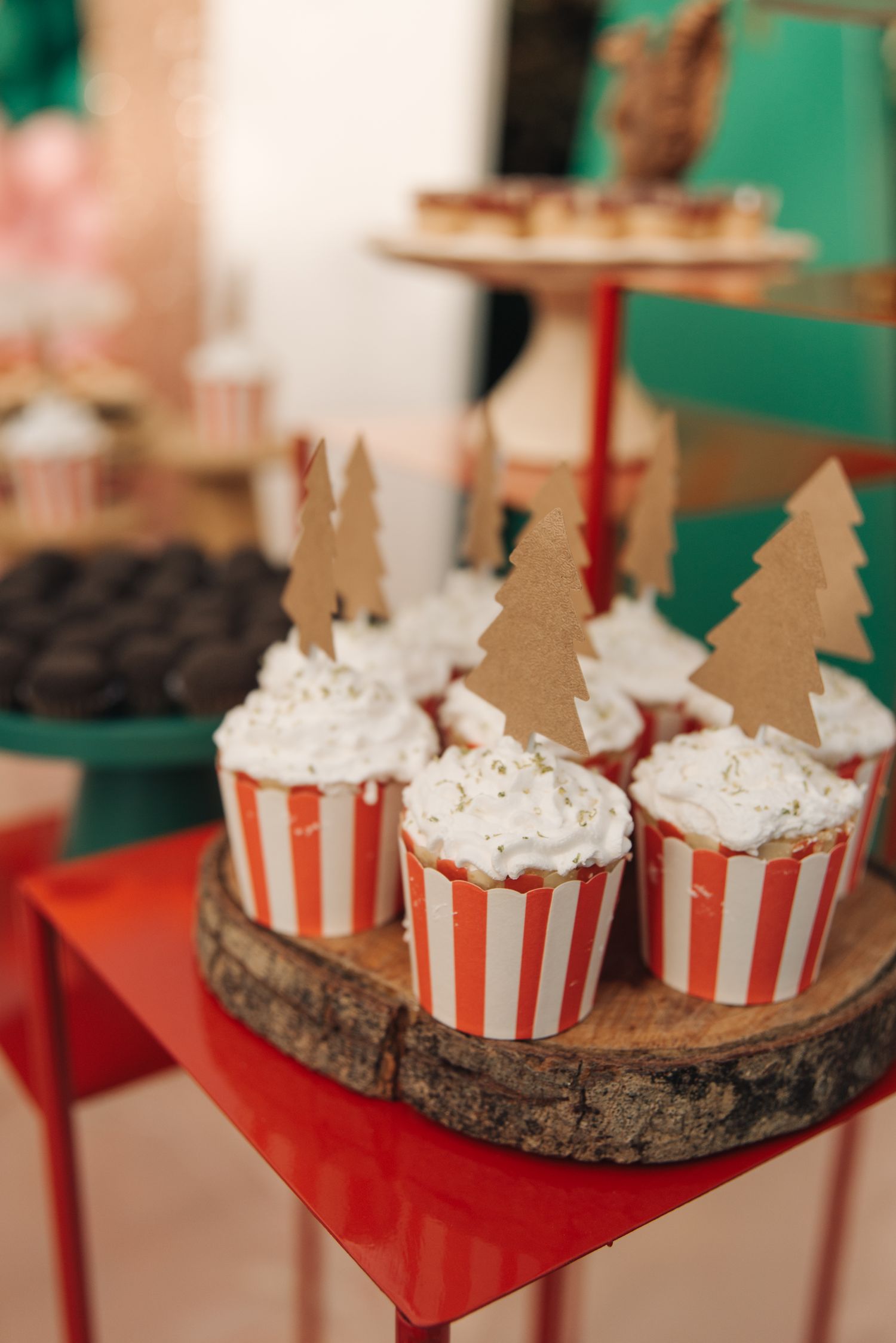 Christmas cupcakes decorated with tree toppers on rustic wood slice stand.