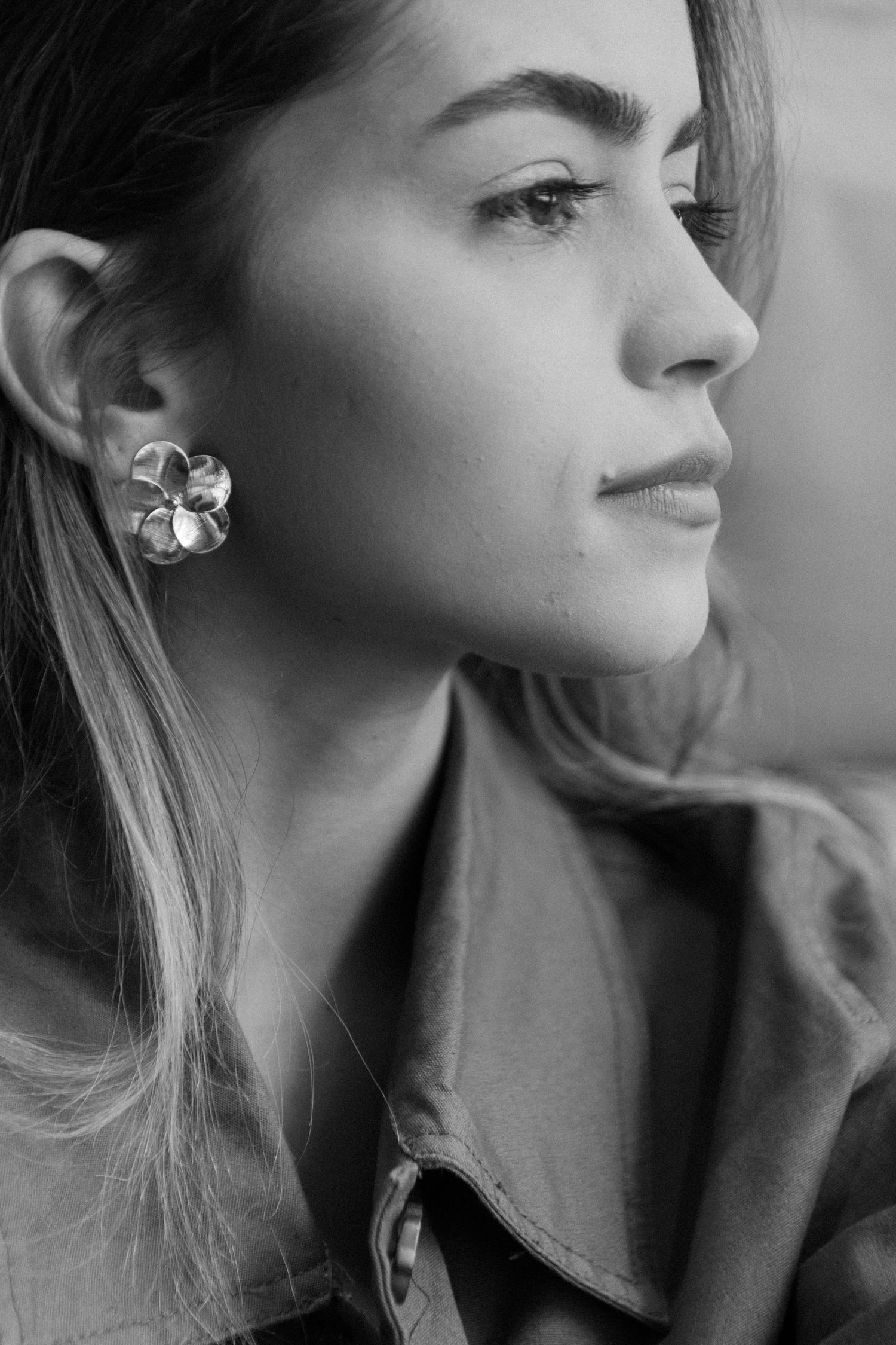 Black and white portrait showing elegant profile view with floral earring in soft lighting.