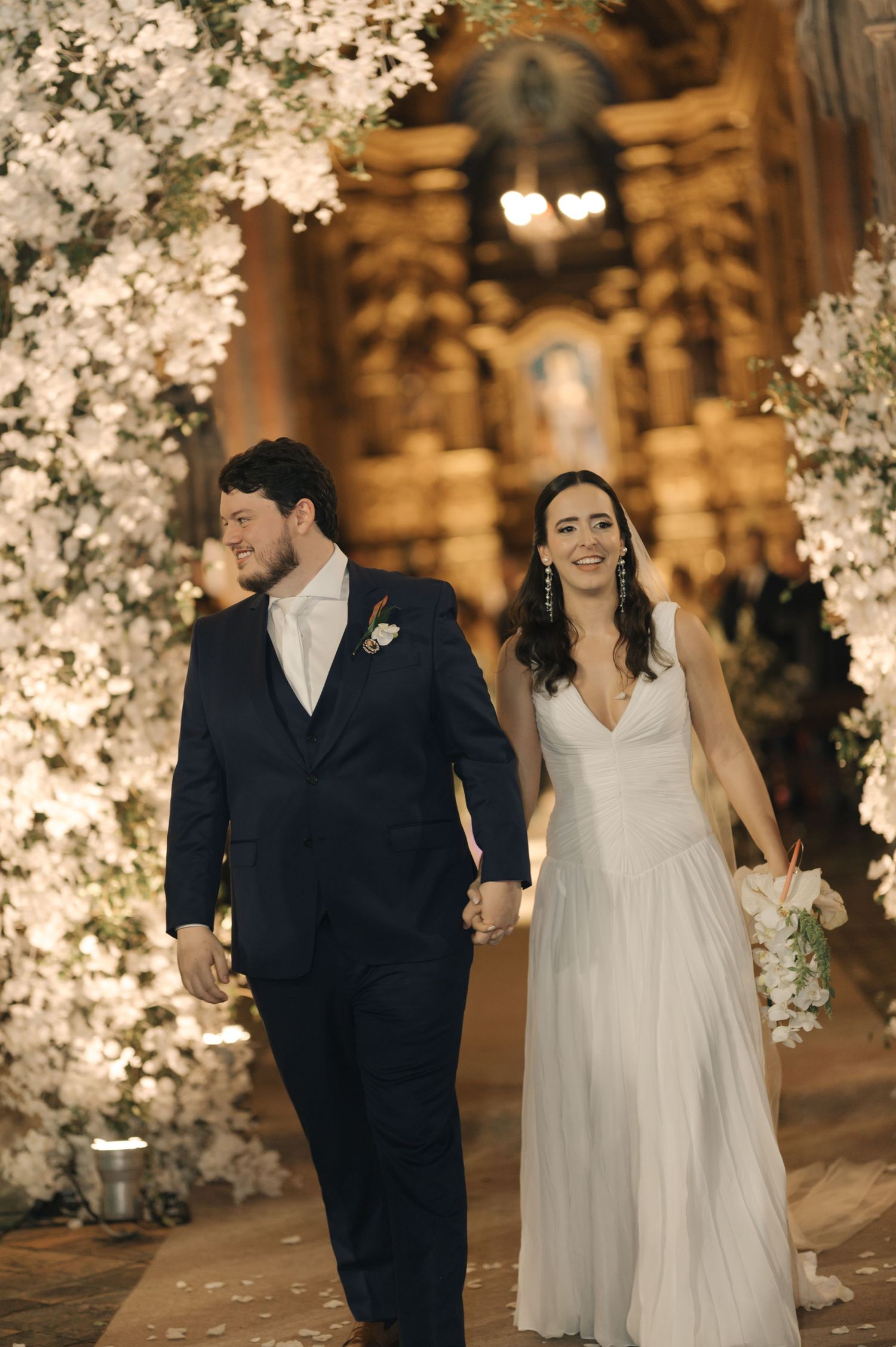 A couple walks together under illuminated cherry blossom trees at an evening wedding celebration.