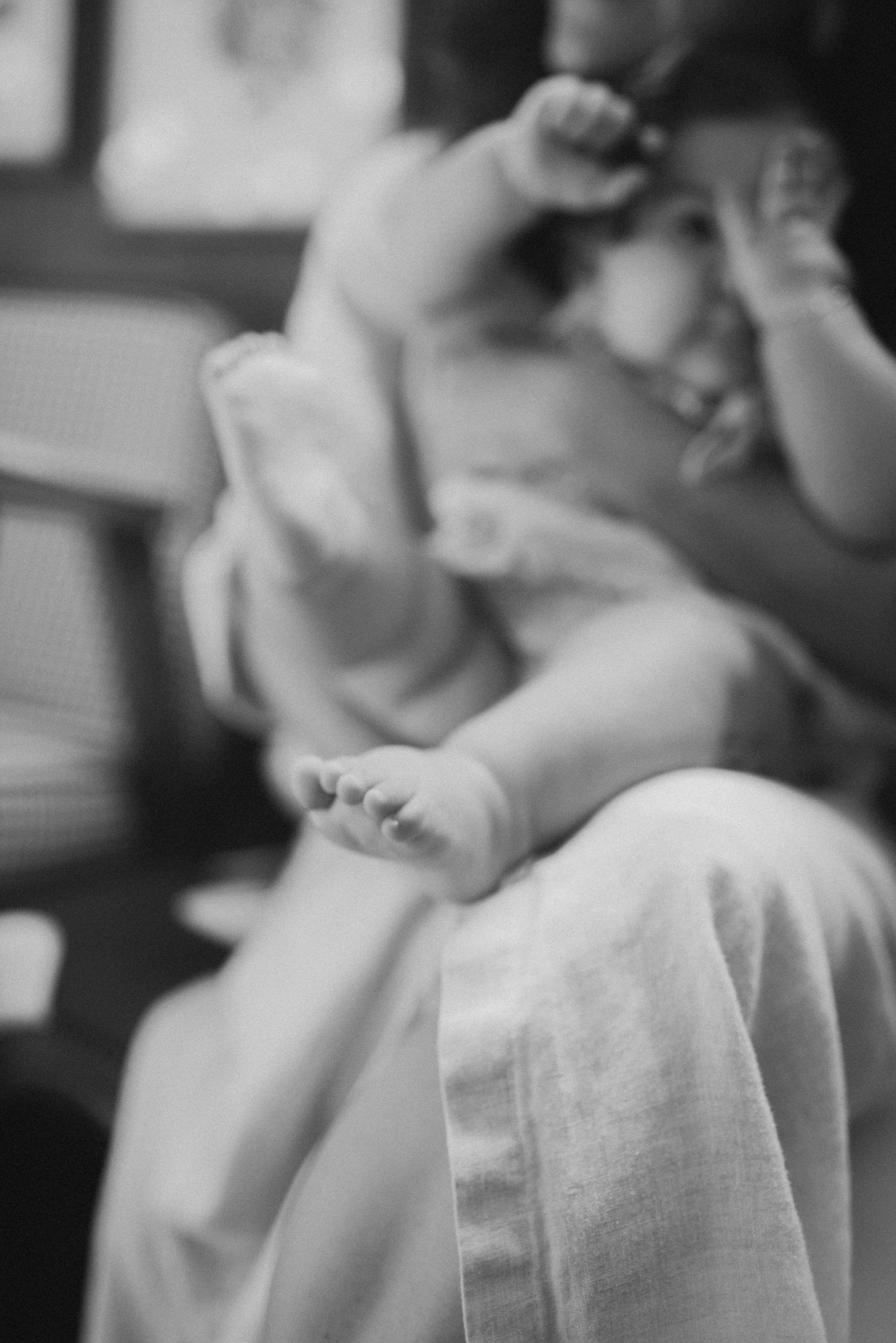 Black and white close-up of tiny baby feet and legs against soft fabric.