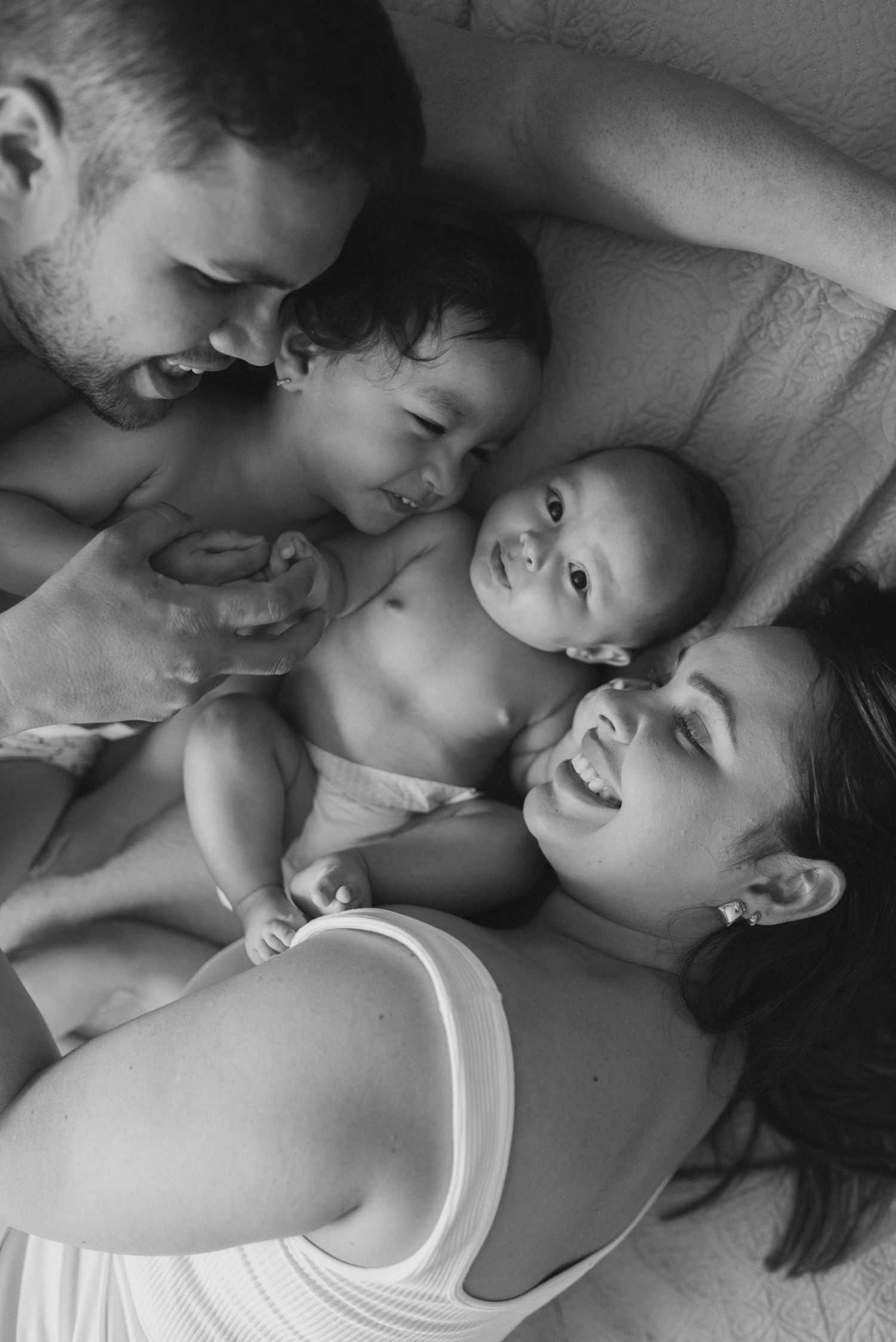 Black and white family portrait showing tender moments of bonding on a bed.