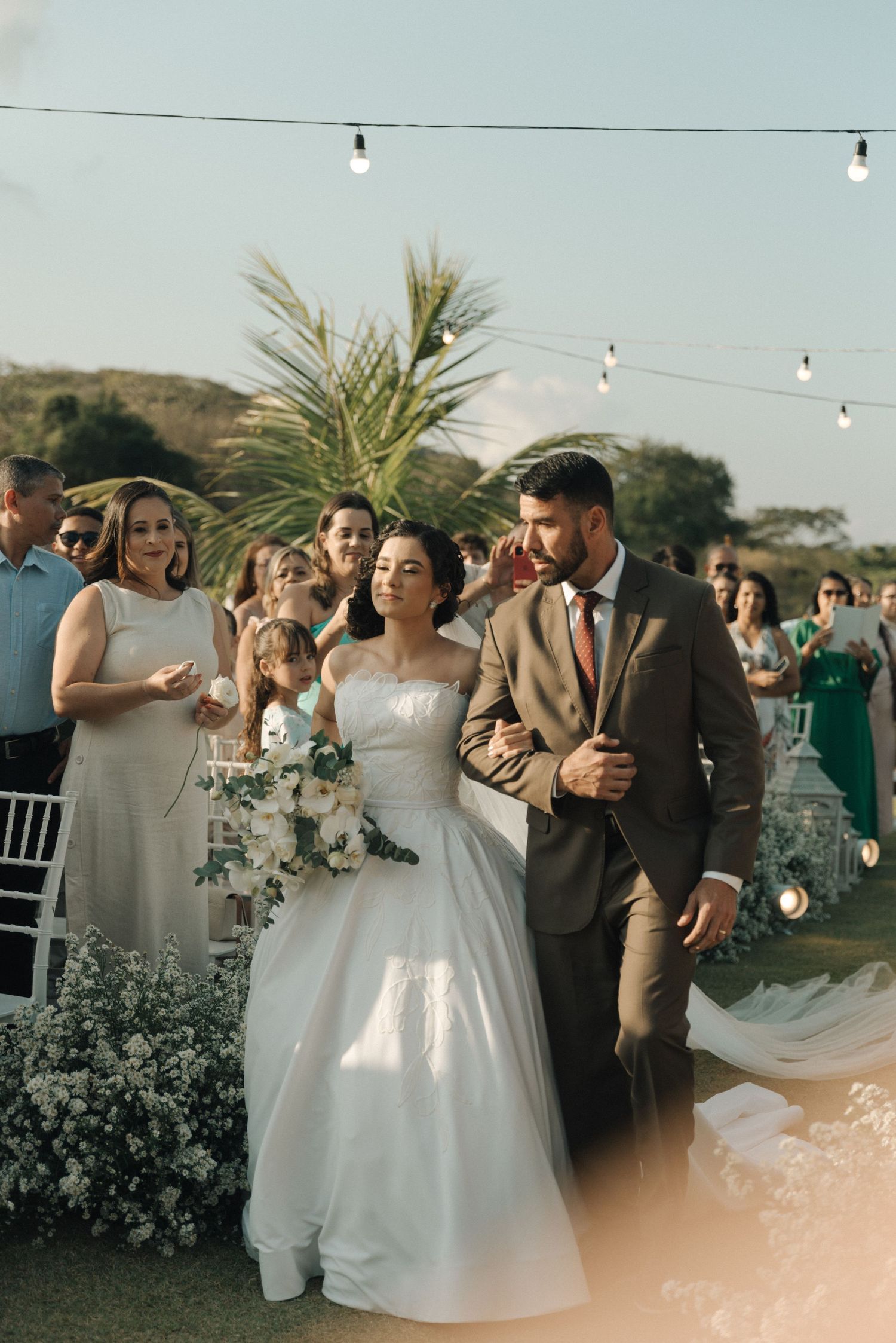 An outdoor wedding ceremony with string lights and palm trees in the background.