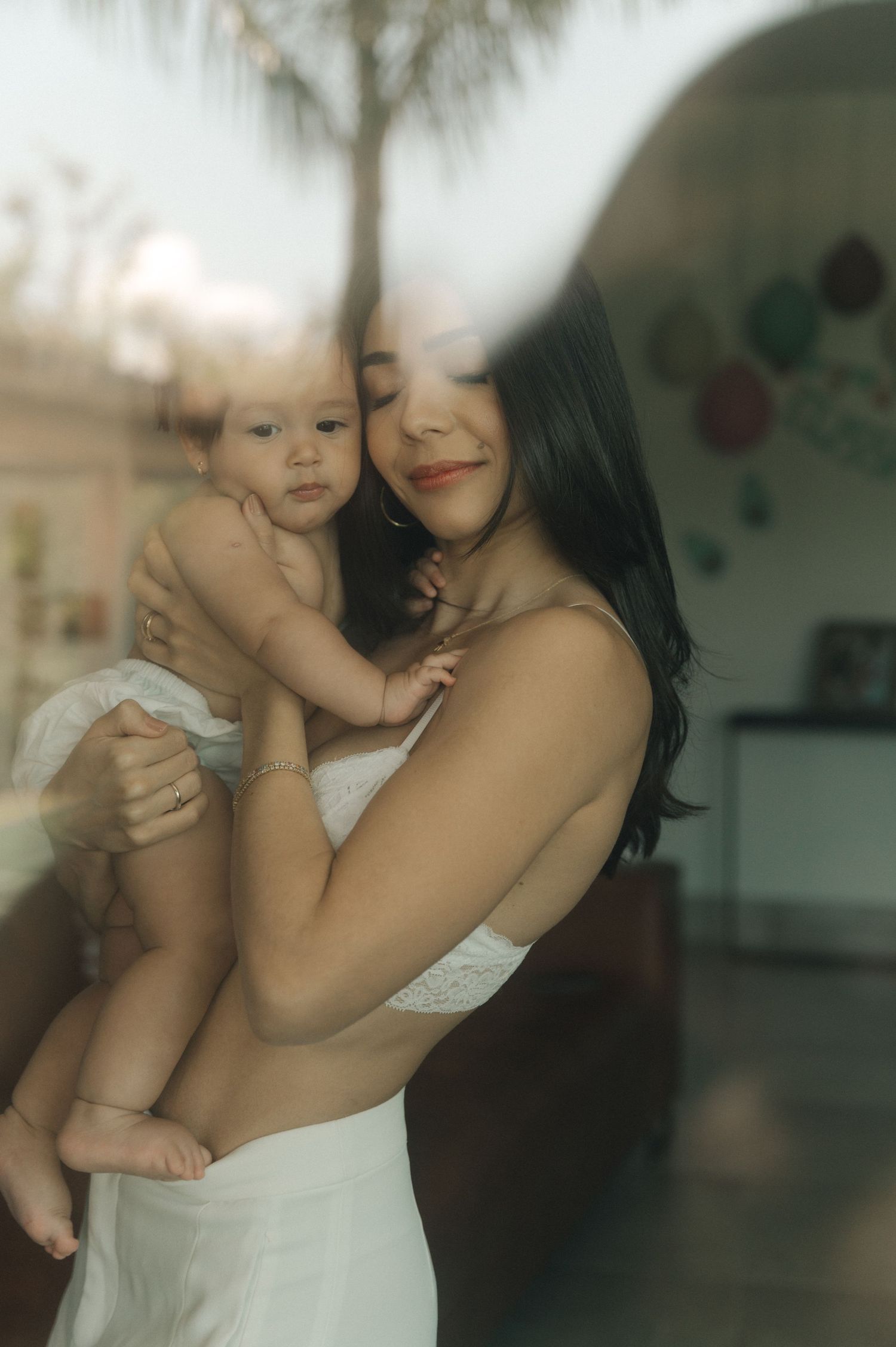 A tender moment captured in soft lighting shows a parent and baby in white clothing sharing an intimate embrace.