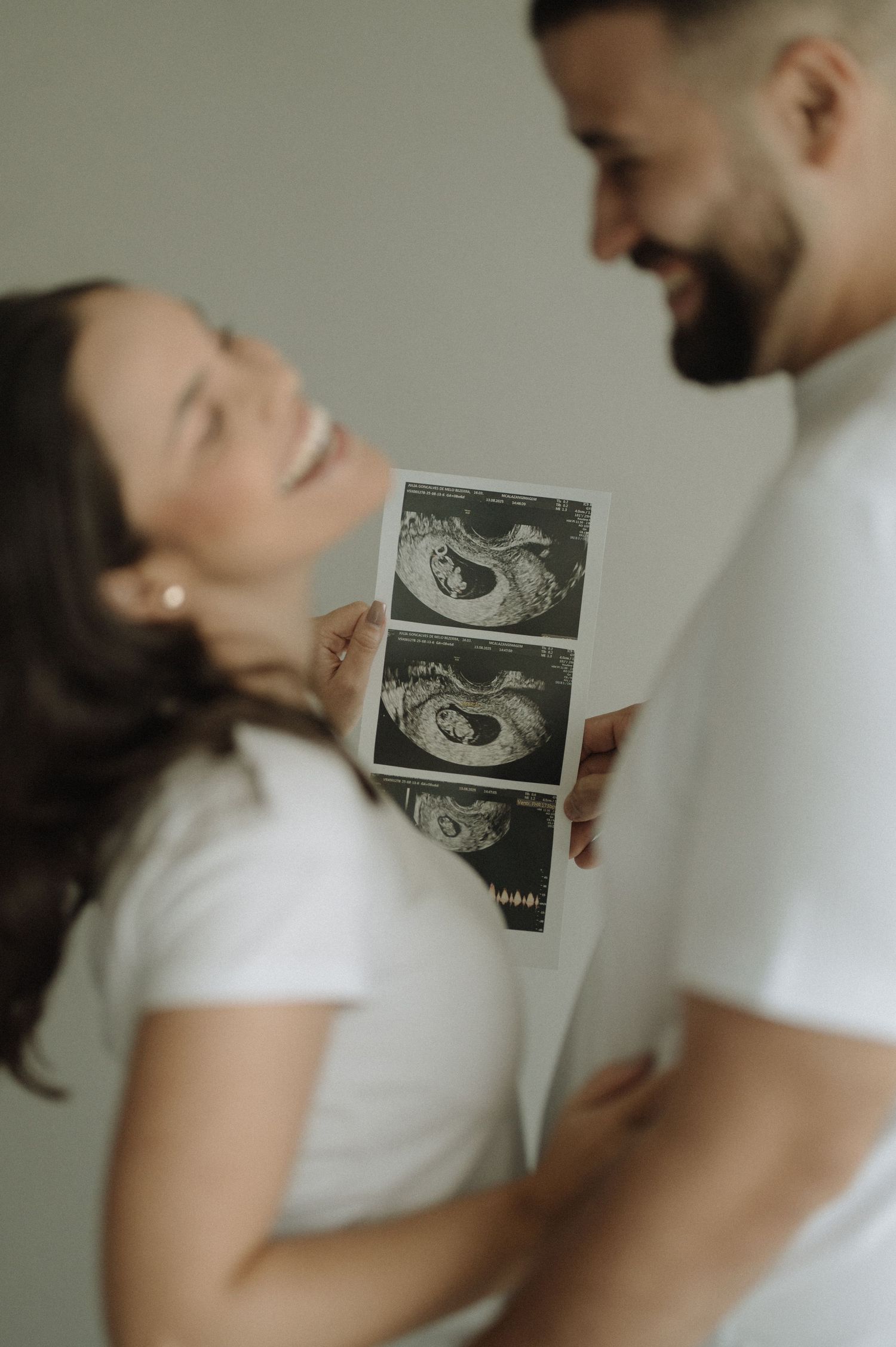 A couple shares a joyful moment while holding ultrasound images of their expected baby.