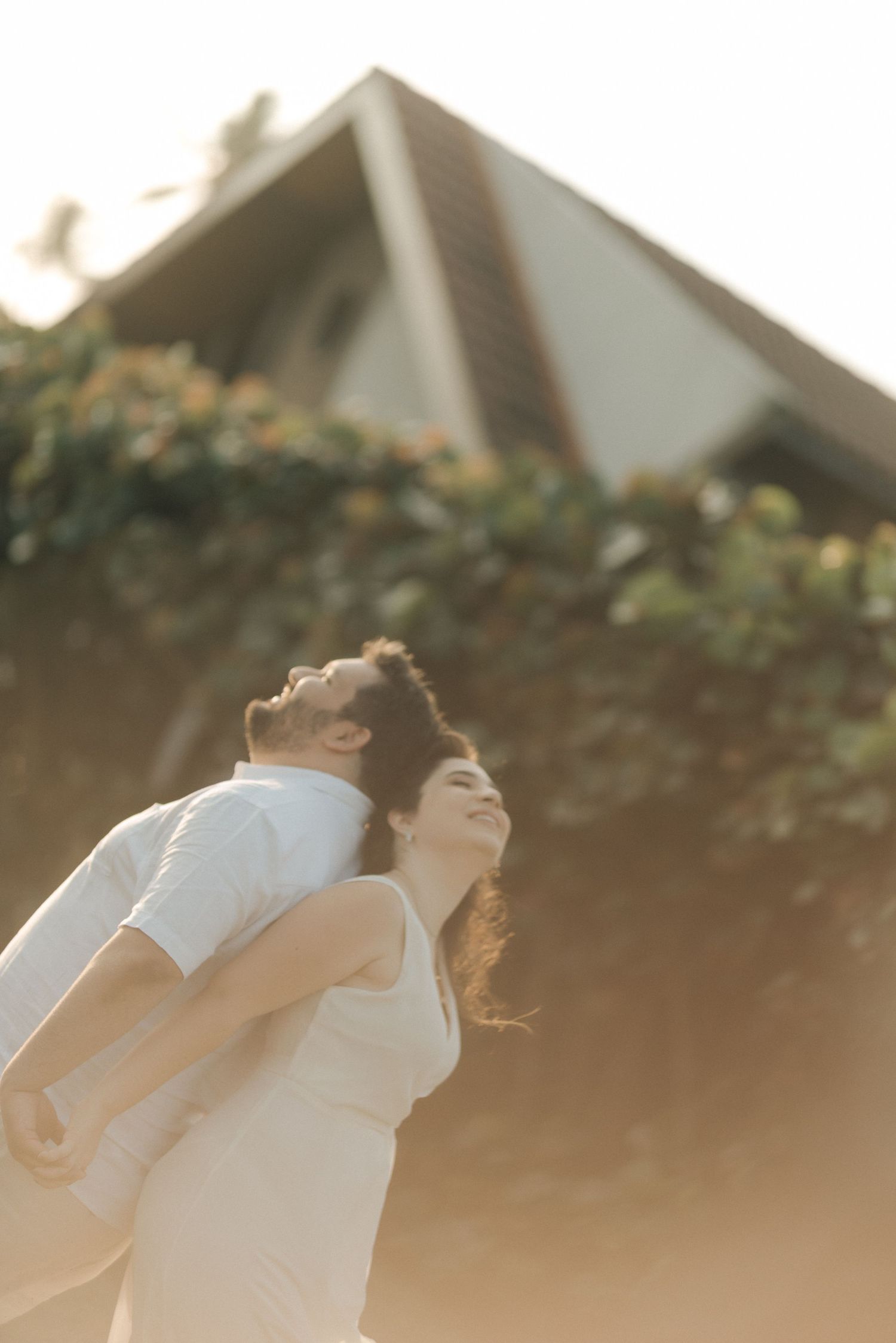 Couple sharing playful moment in sunset light with architectural background.
