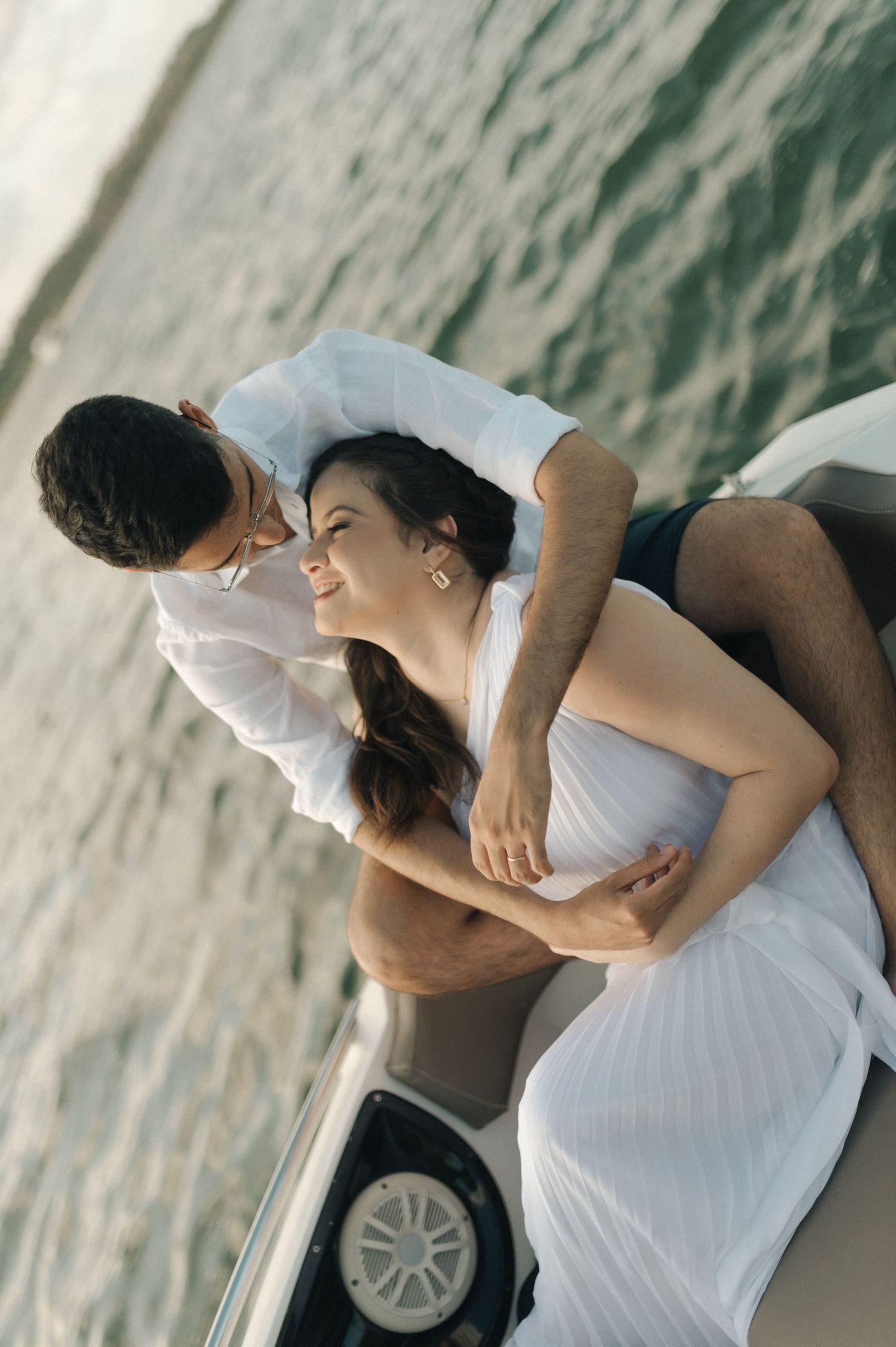 A couple in white clothing share a romantic moment on a boat.