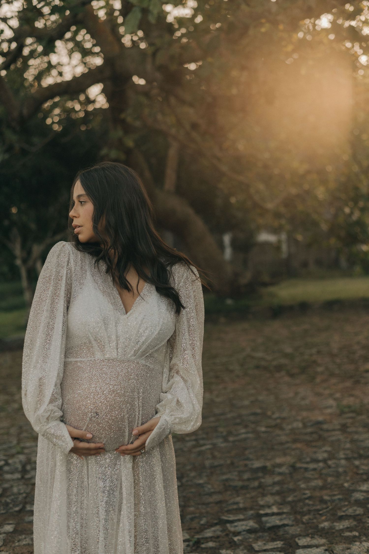 Ethereal maternity portrait of woman in white dress during golden hour.