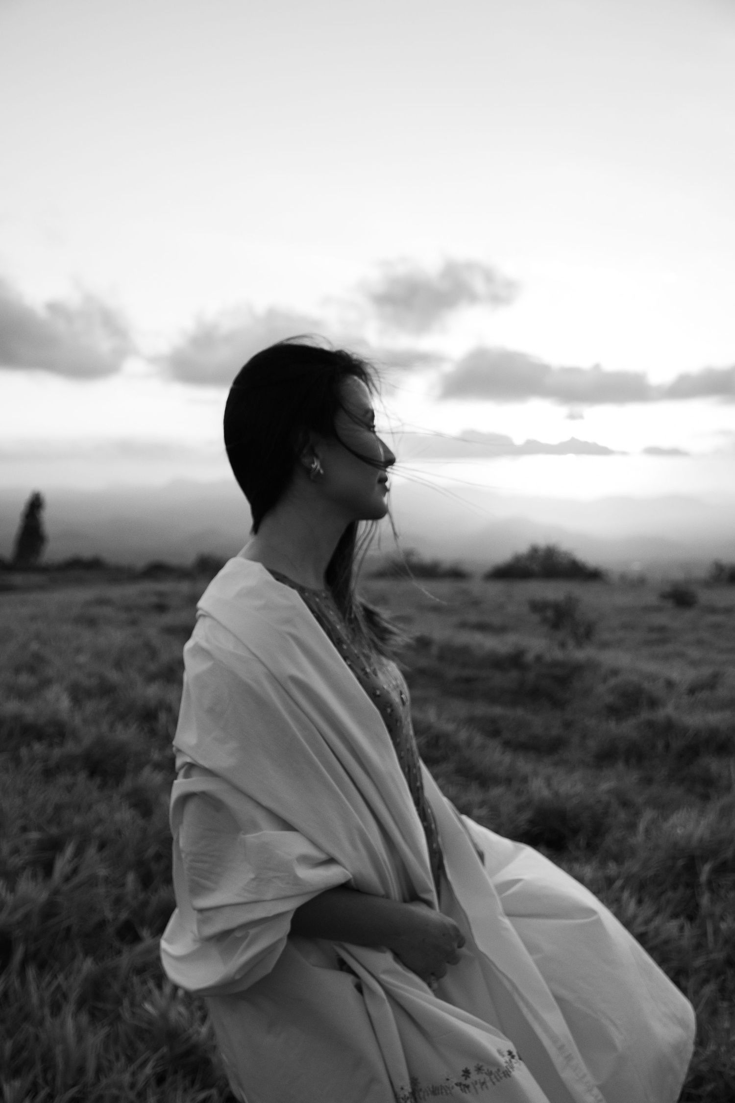 Silhouette in white dress against sunset sky in dramatic black and white landscape.