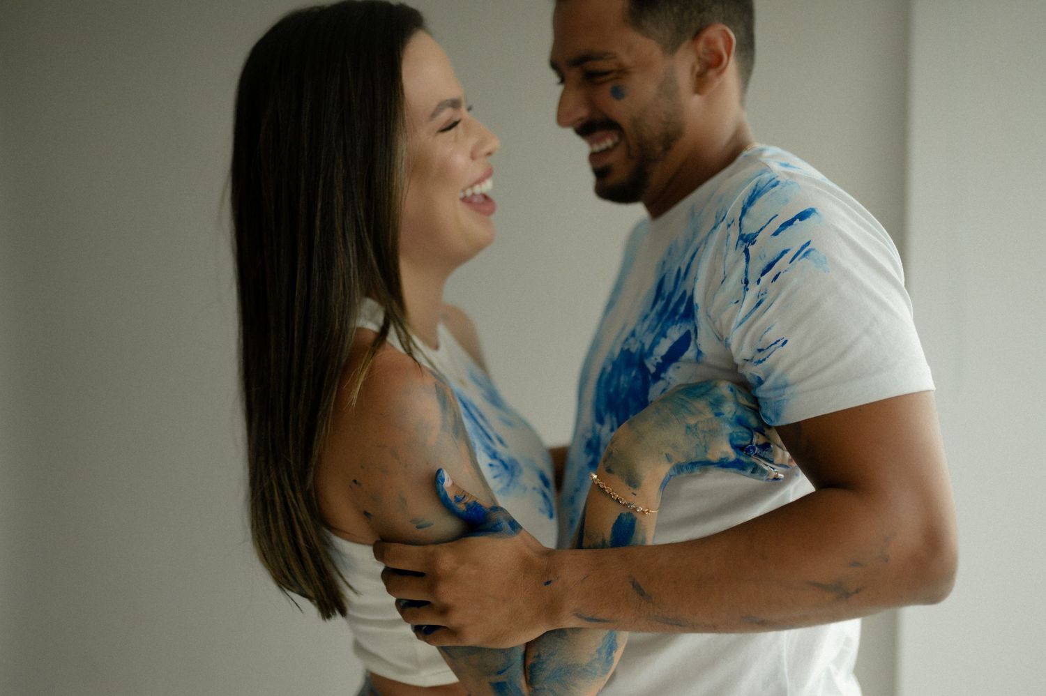 A couple wearing paint-splattered white t-shirts laughs together during a playful moment.