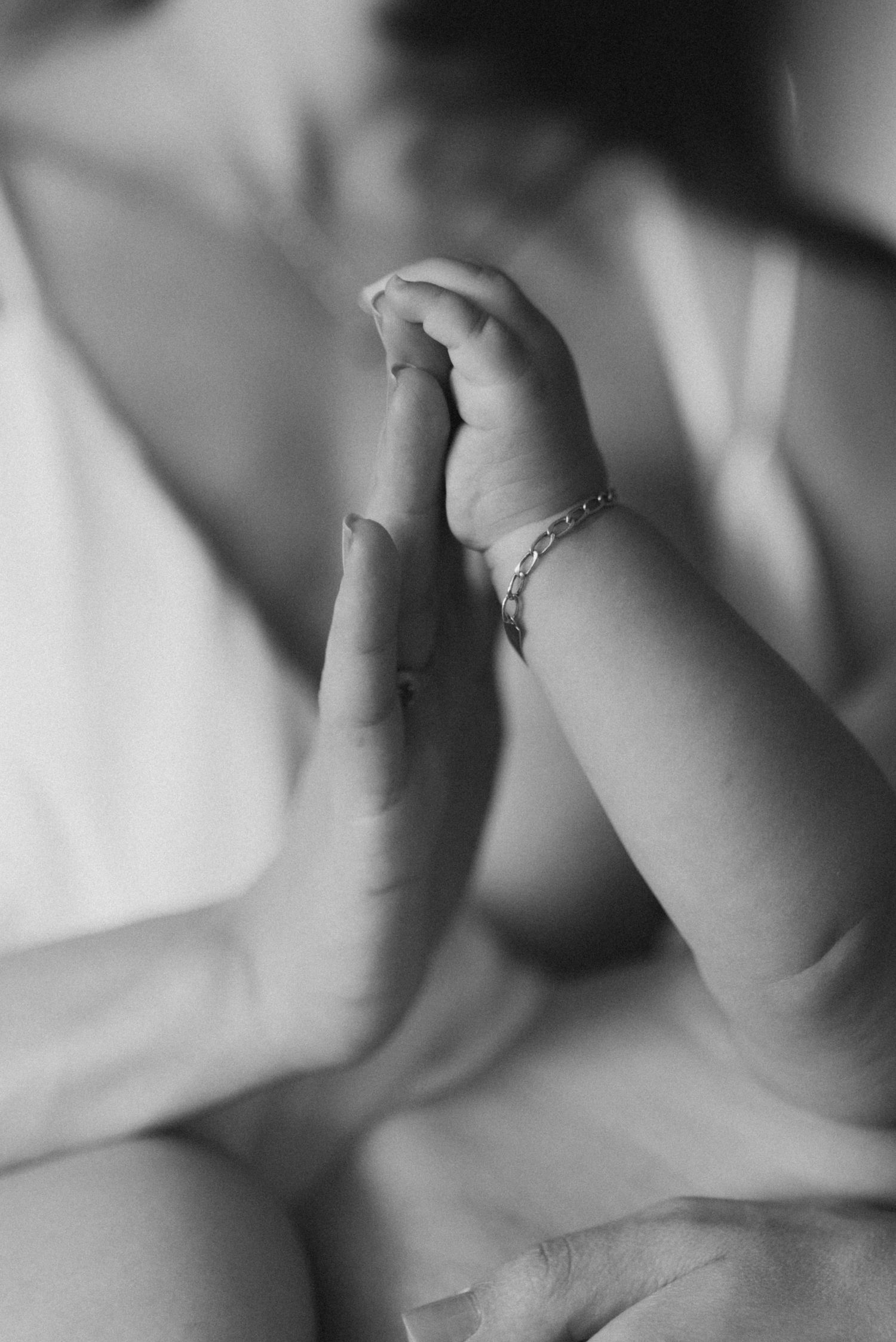 A black and white close-up photograph of a baby's tiny hand wearing a delicate bracelet.
