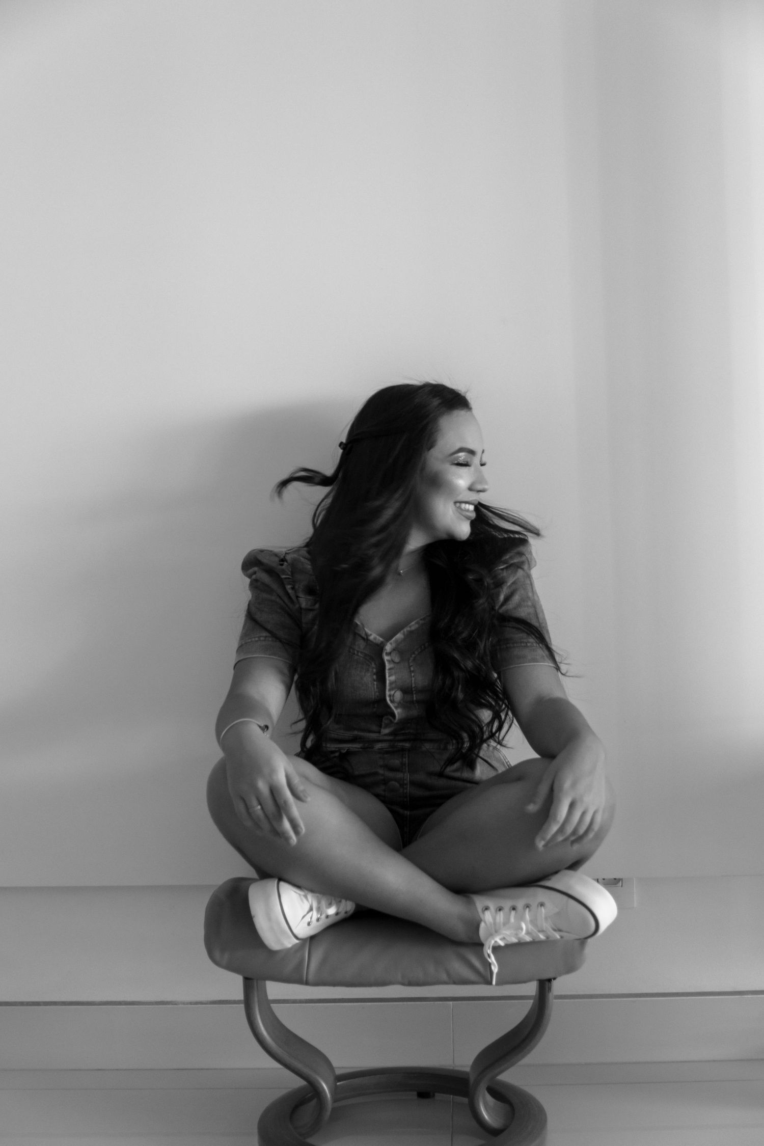 Casual portrait on decorative chair shows natural joy against minimalist background.