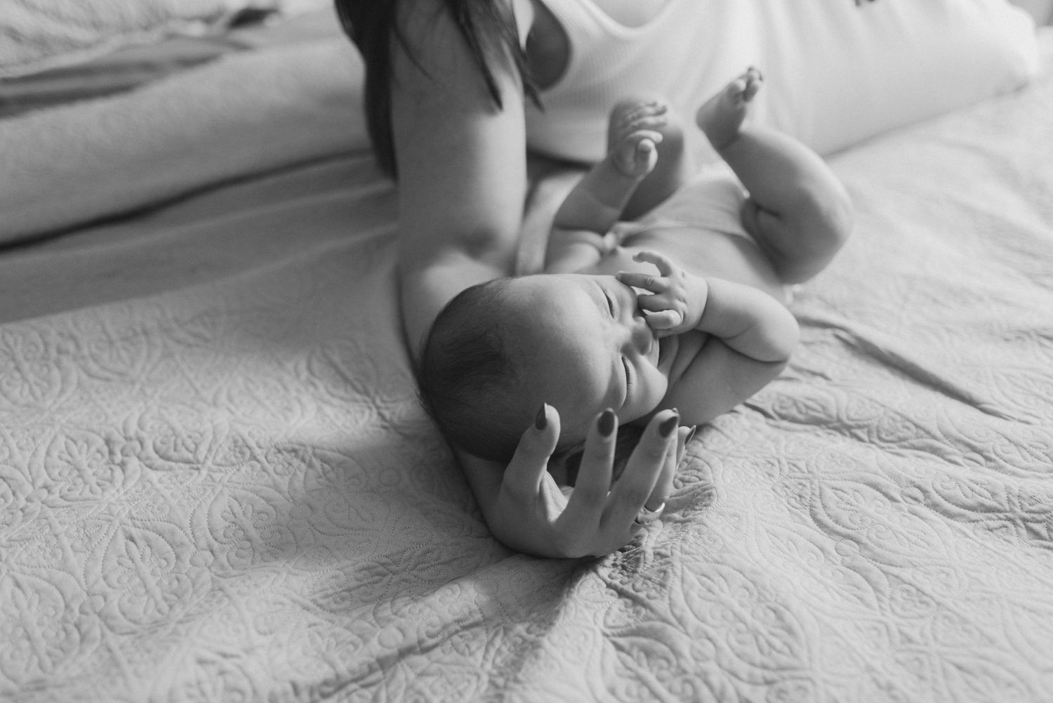 Black and white image of a baby lying on textured bedding during an intimate photo session.