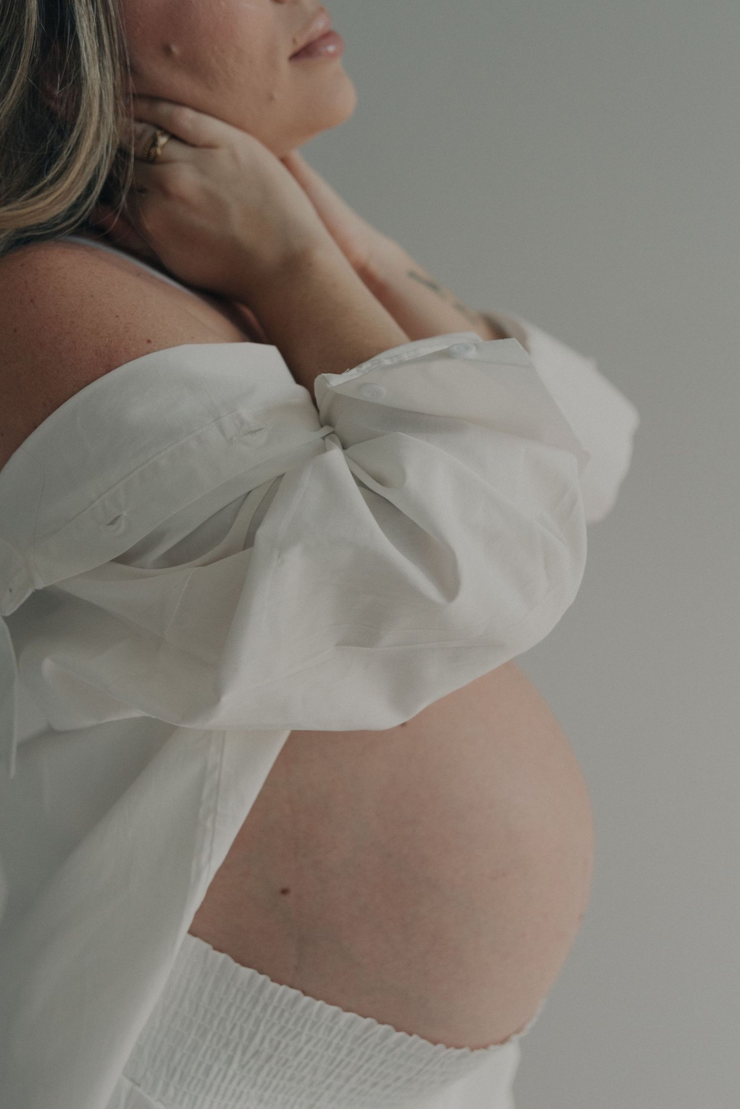 Side profile maternity photo with flowing white fabric highlighting the pregnant belly.