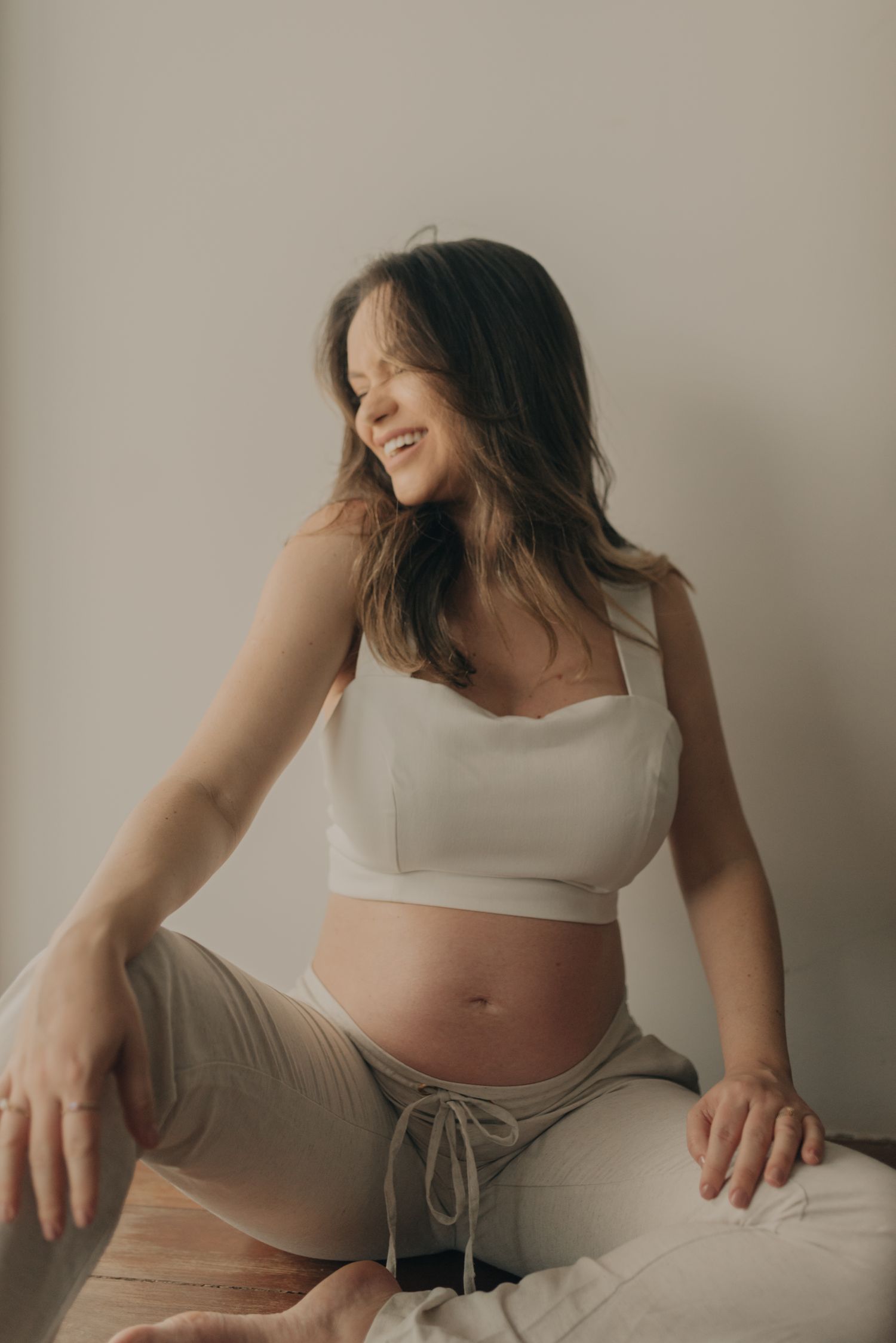 Casual maternity portrait showing expectant figure in white crop top and drawstring pants.