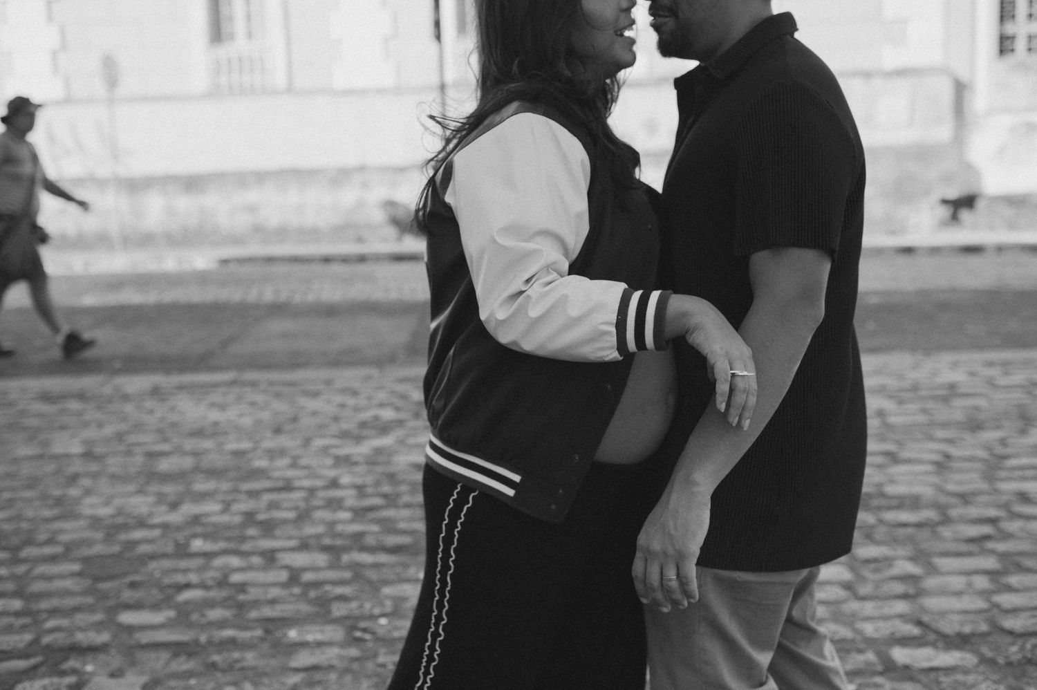 Black and white candid moment of couple in casual attire on cobblestone street.