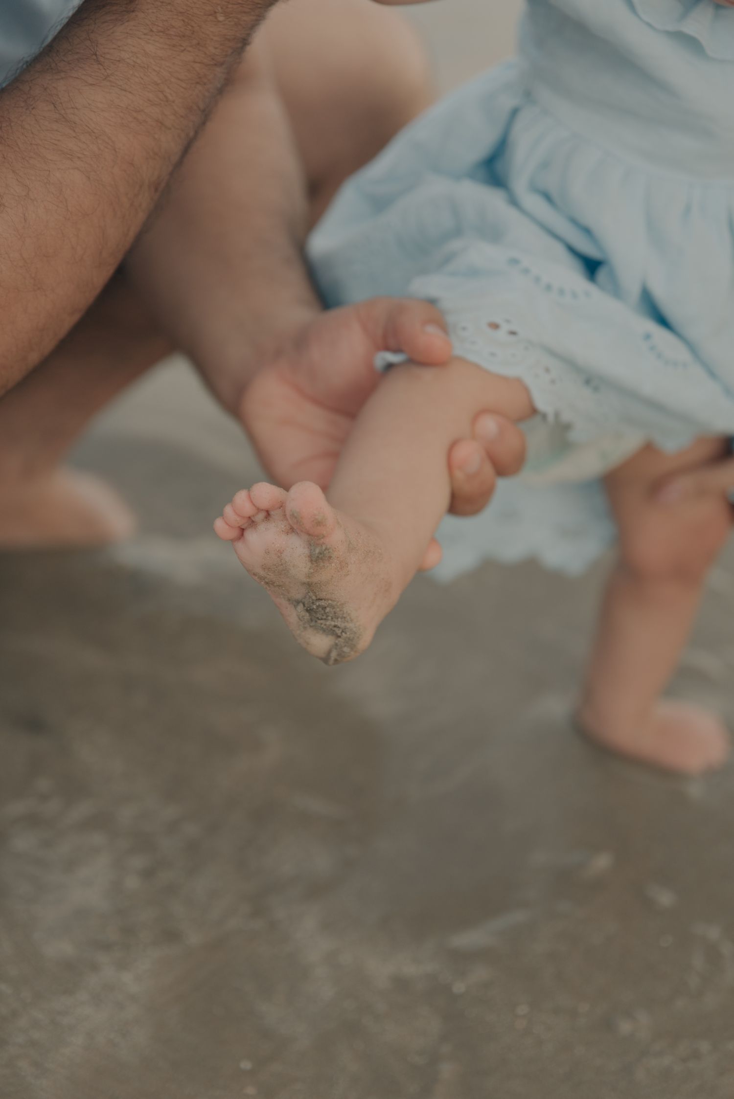 Close-up of sandy baby feet at the beach with waves in soft focus.