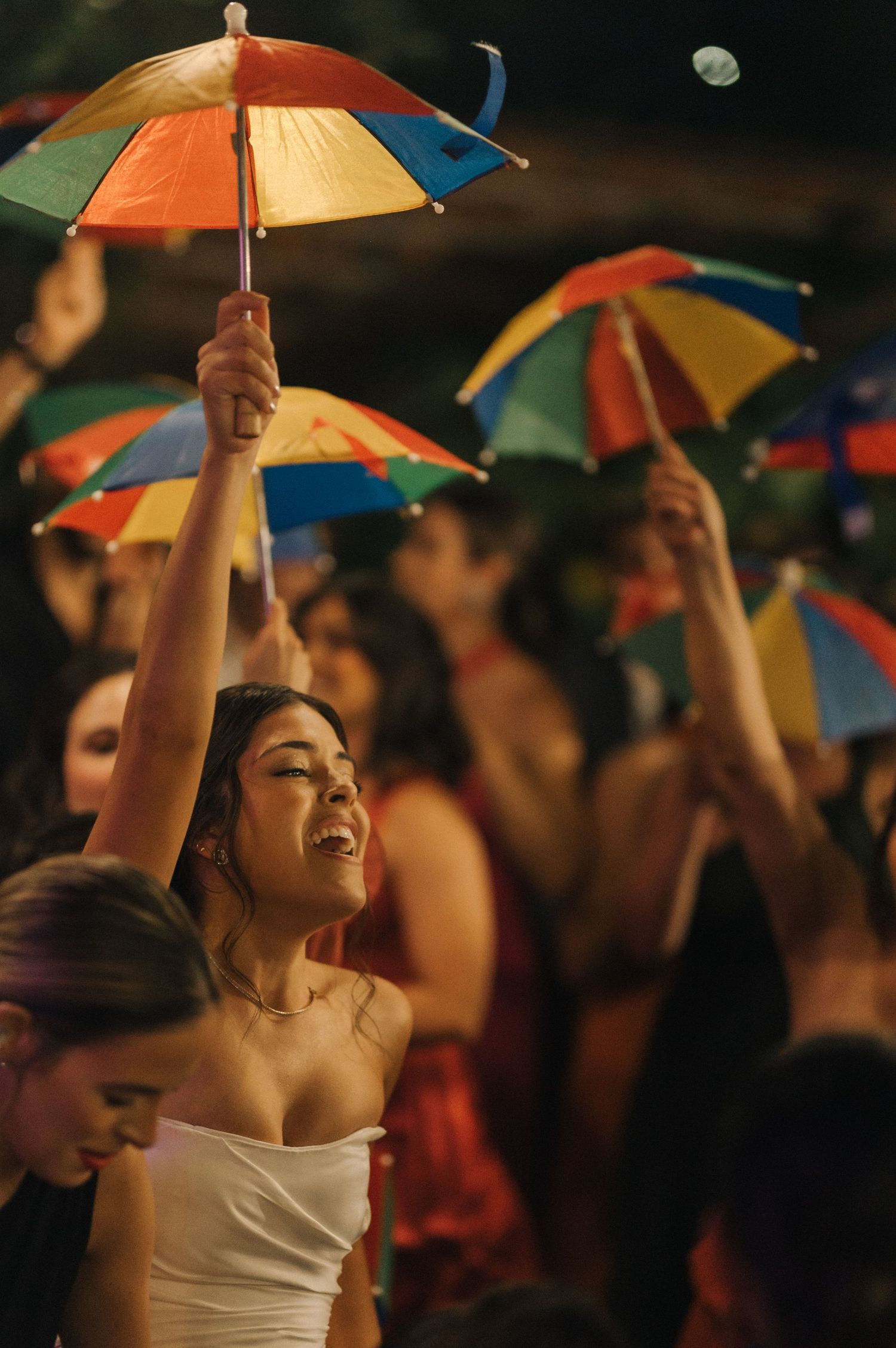 A bride joyfully lifts a colorful umbrella during a nighttime wedding reception.
