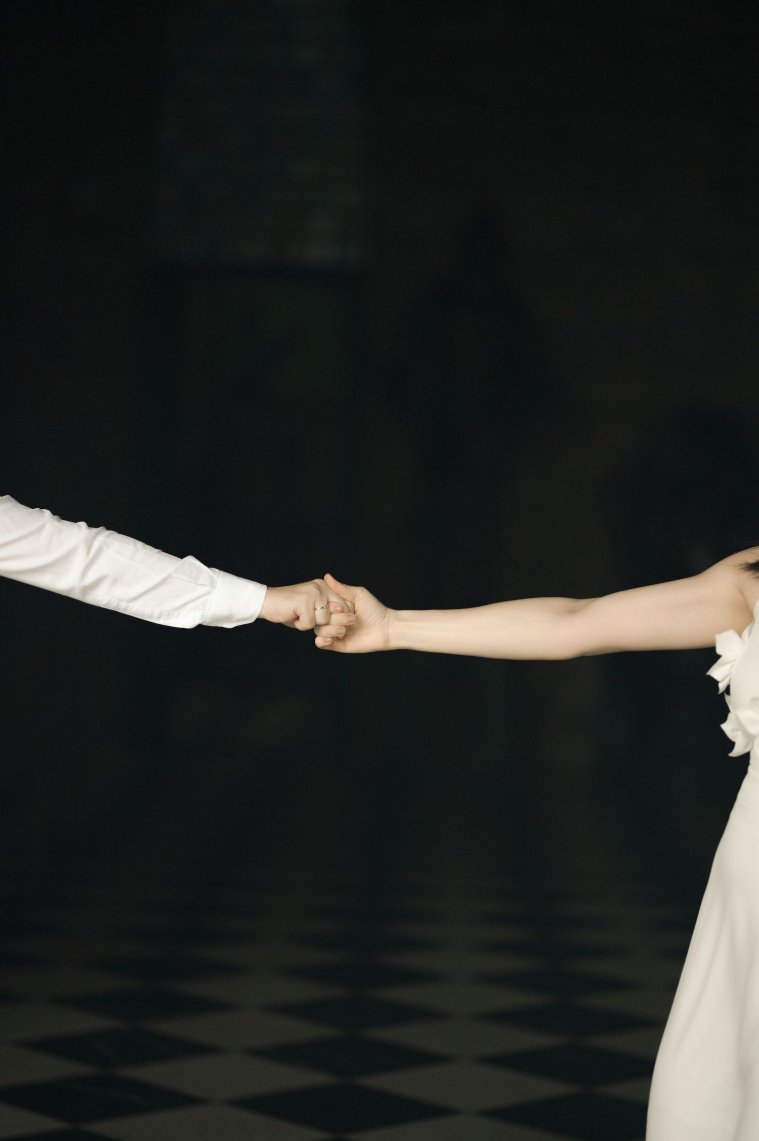 Two hands reaching out to hold each other against a dark background with a checkered floor.