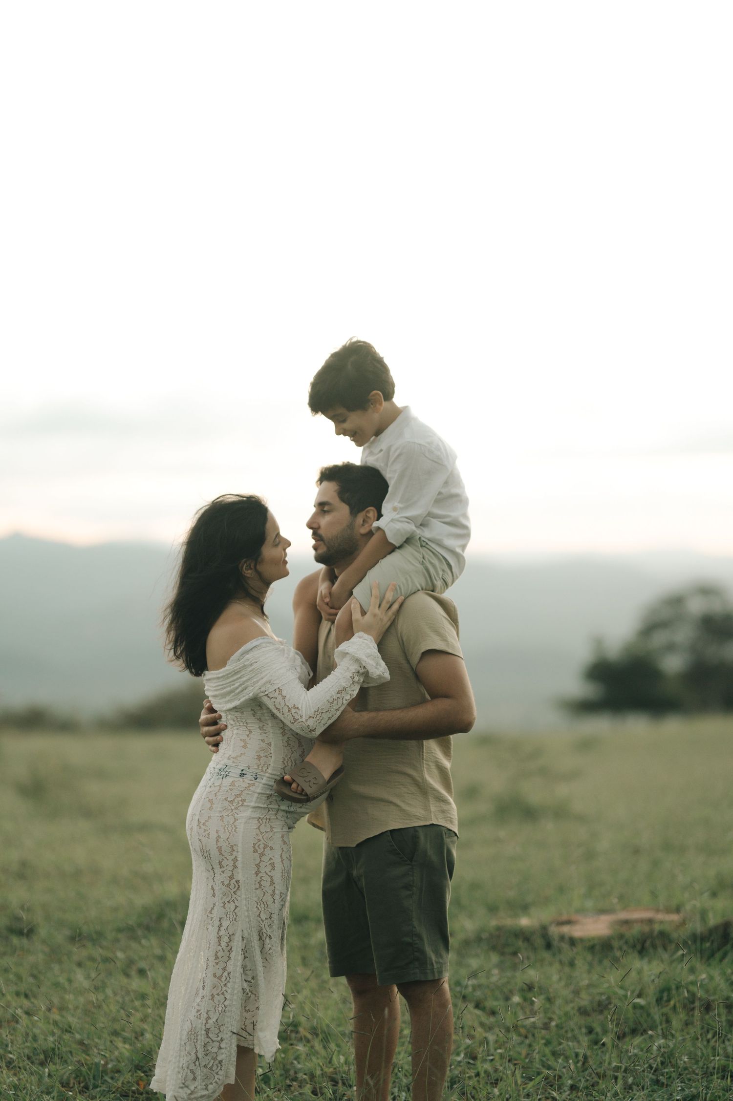A romantic couple embraces in a green meadow at sunset wearing white dress and casual attire.