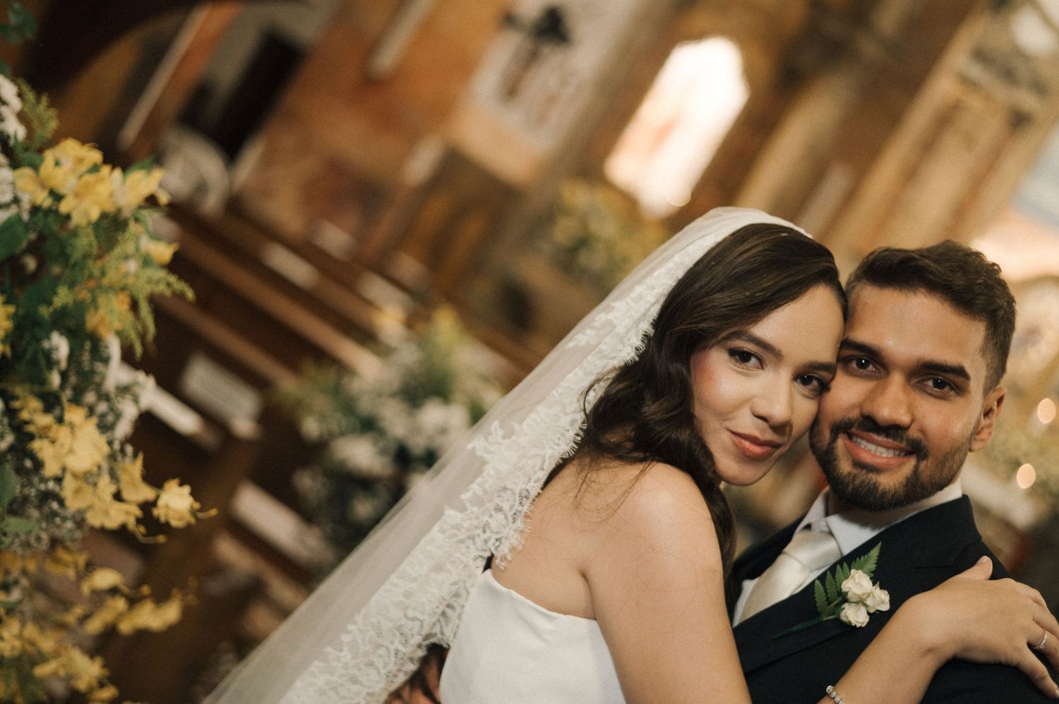 Happy bride and groom pose together in ornate church after wedding ceremony, bride wearing lace veil.