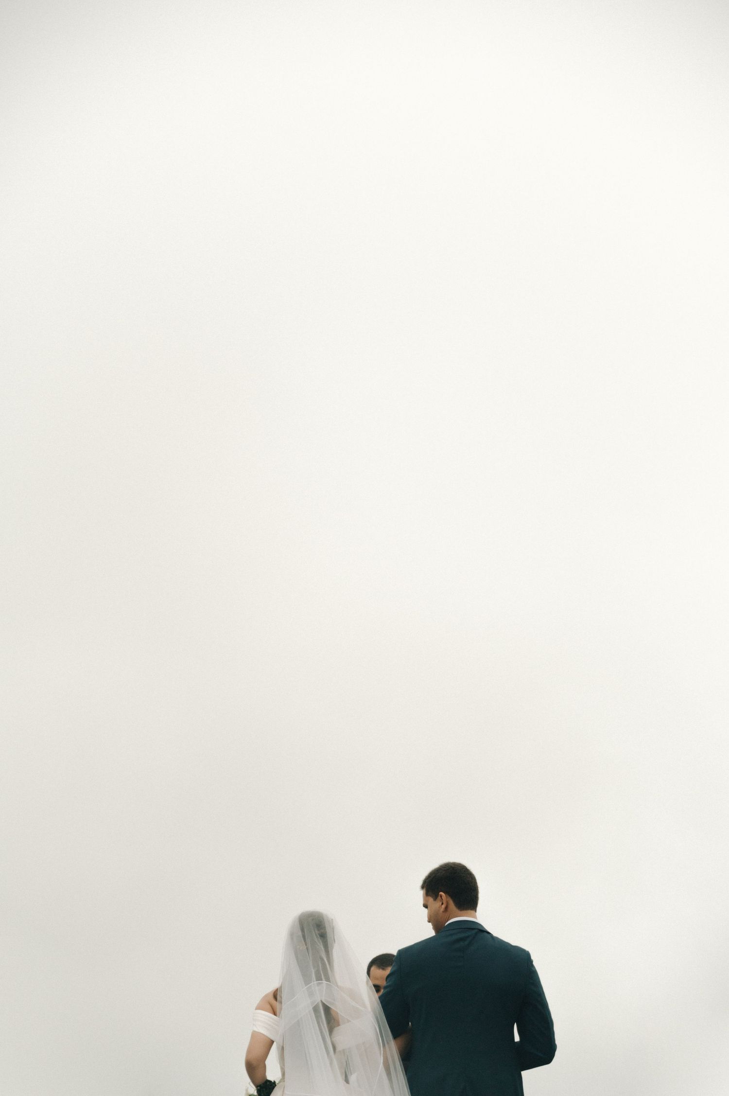 Minimalist wedding photo showing a couple walking with a black umbrella against a white background.