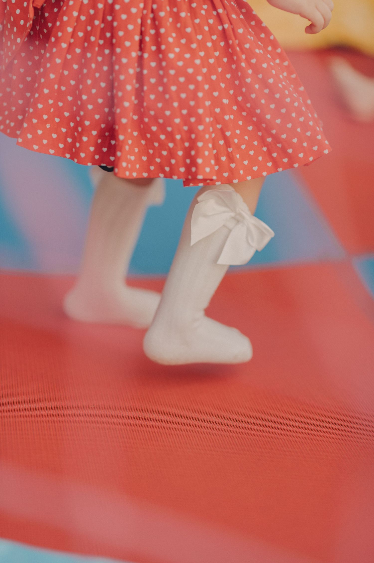 Close-up view of white stockings with bow detail and red polka dot dress hem against a coral background.