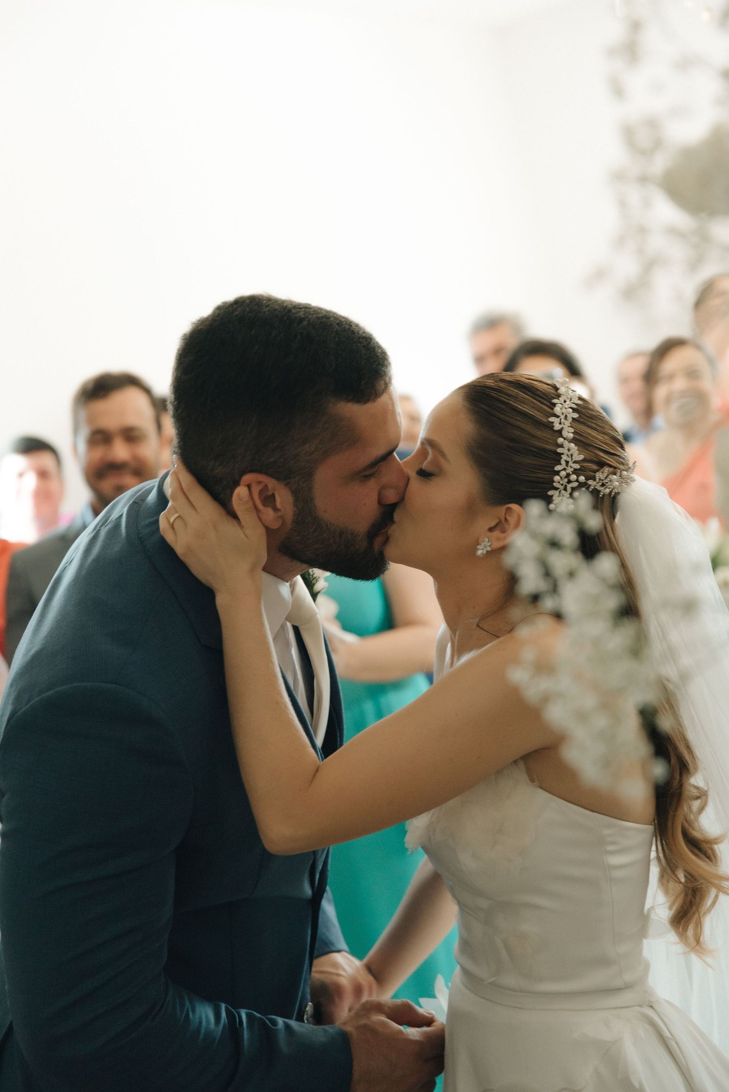 Newlyweds share their first kiss as guests celebrate in the background during a wedding ceremony.