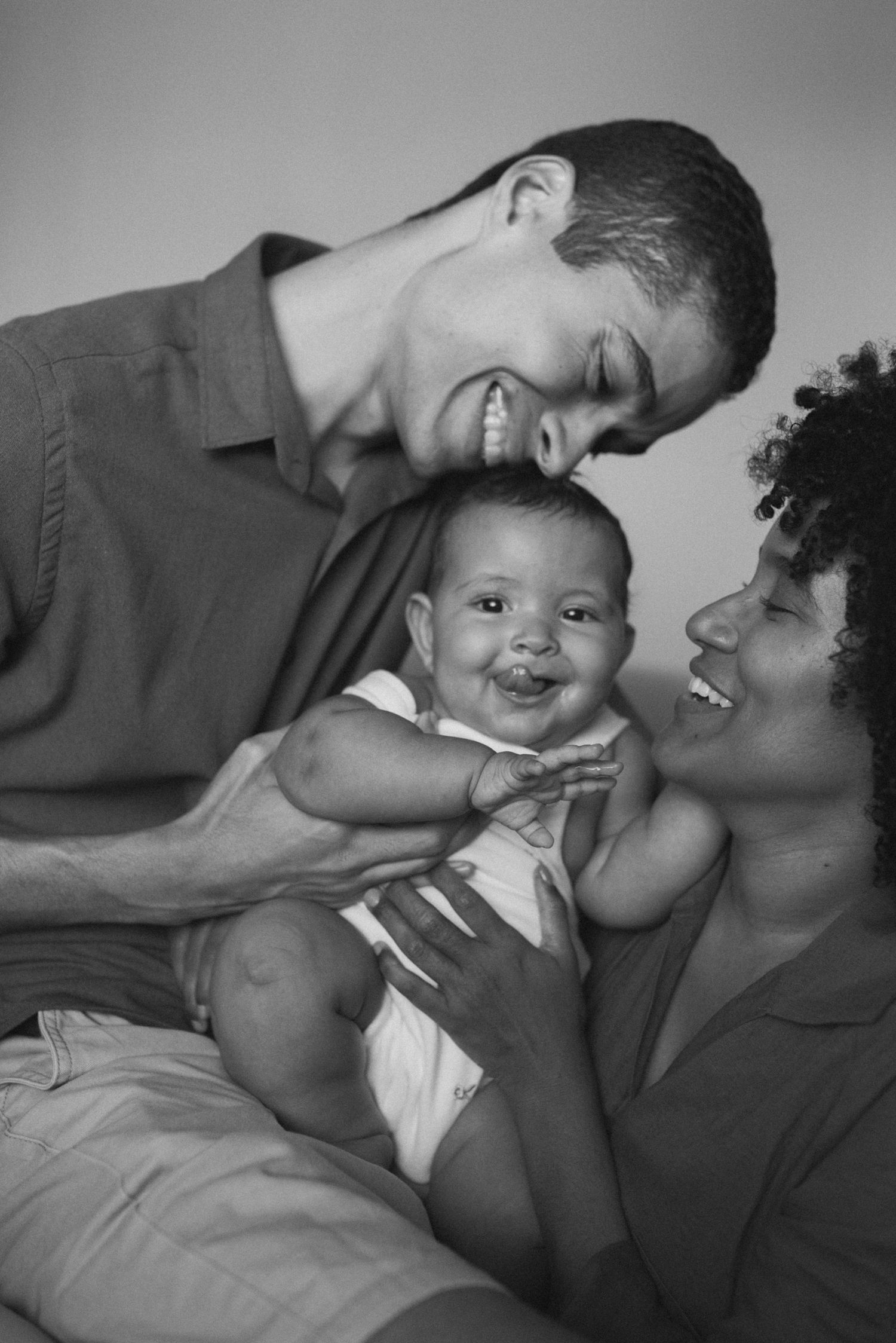 A loving family moment with parents and their laughing baby in black and white.