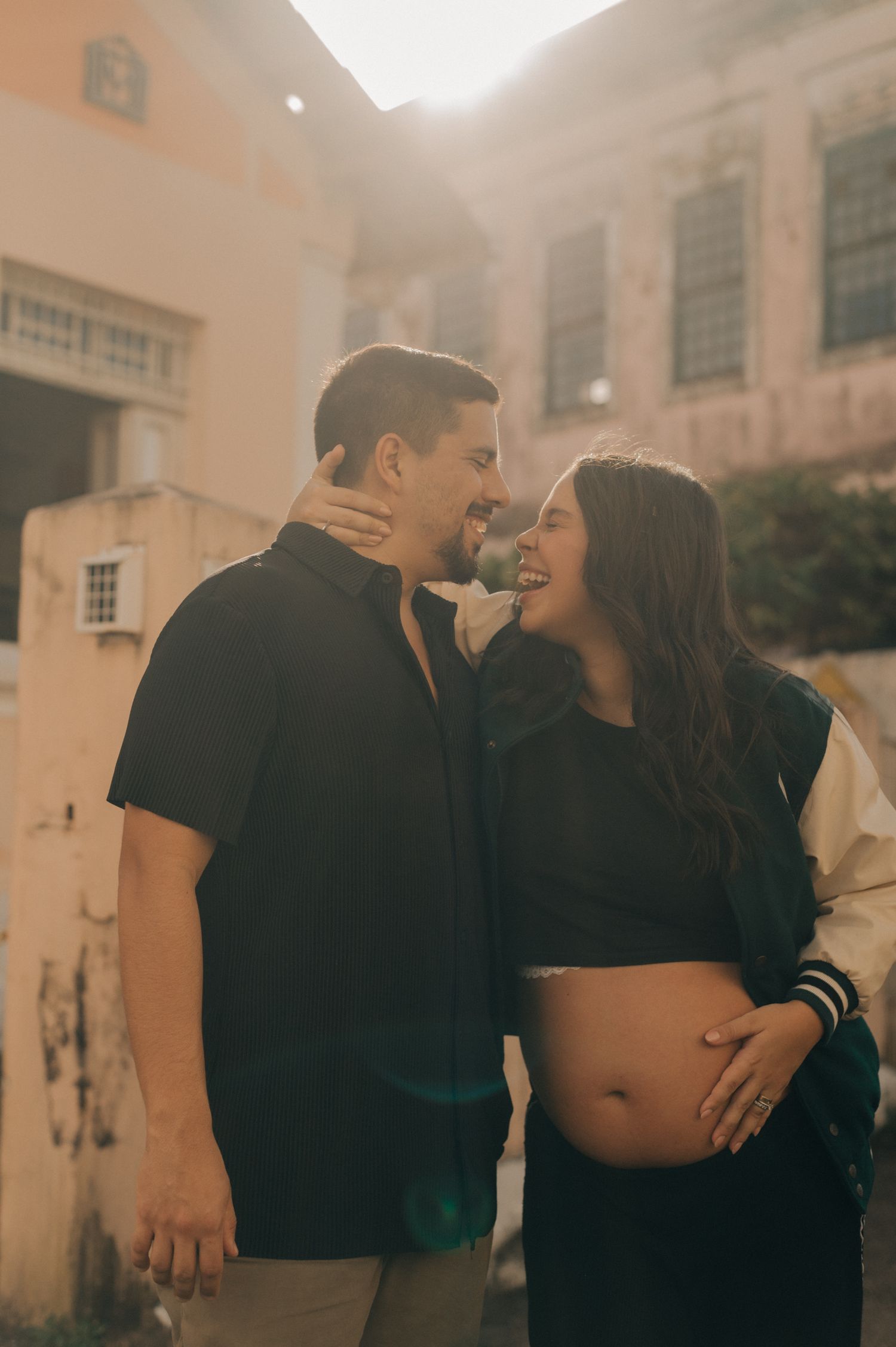 A loving couple sharing an intimate moment against a sunlit building backdrop.