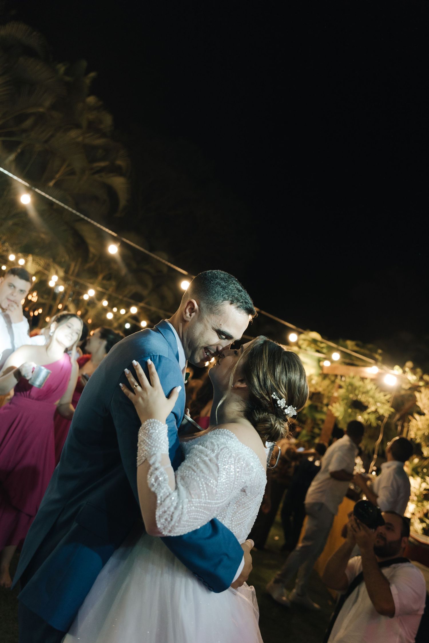 A couple shares their first dance under string lights at an outdoor evening reception.