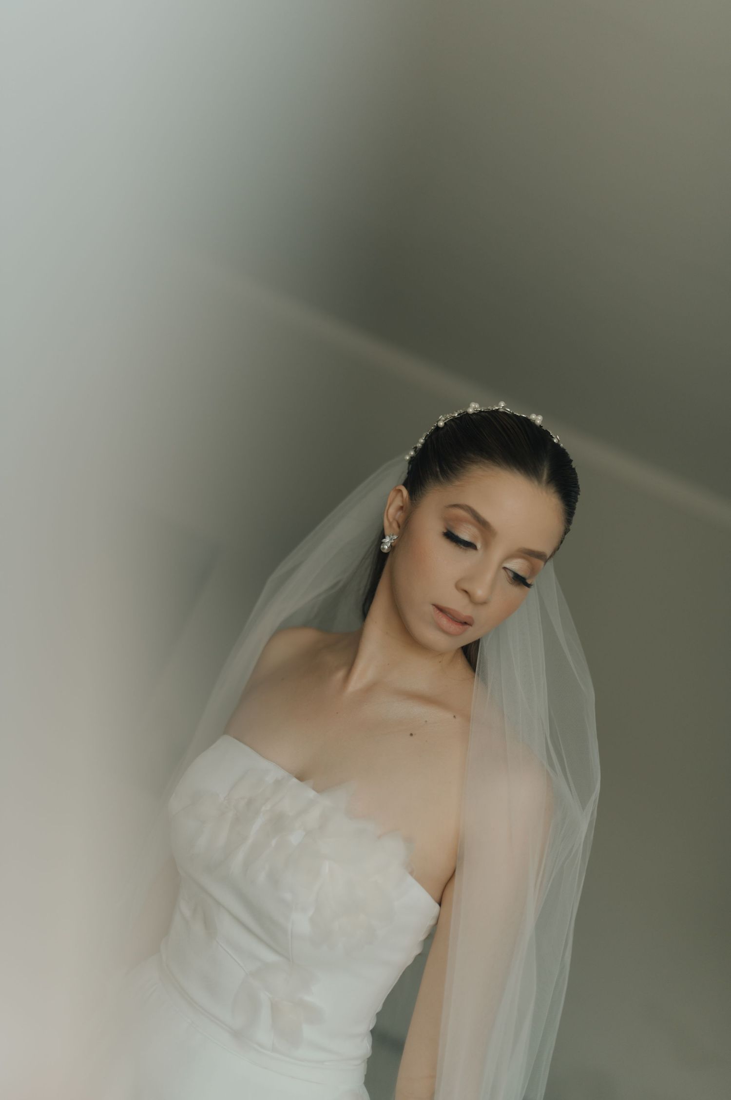 A serene bridal portrait featuring a strapless white wedding gown and flowing veil in soft, ethereal lighting.