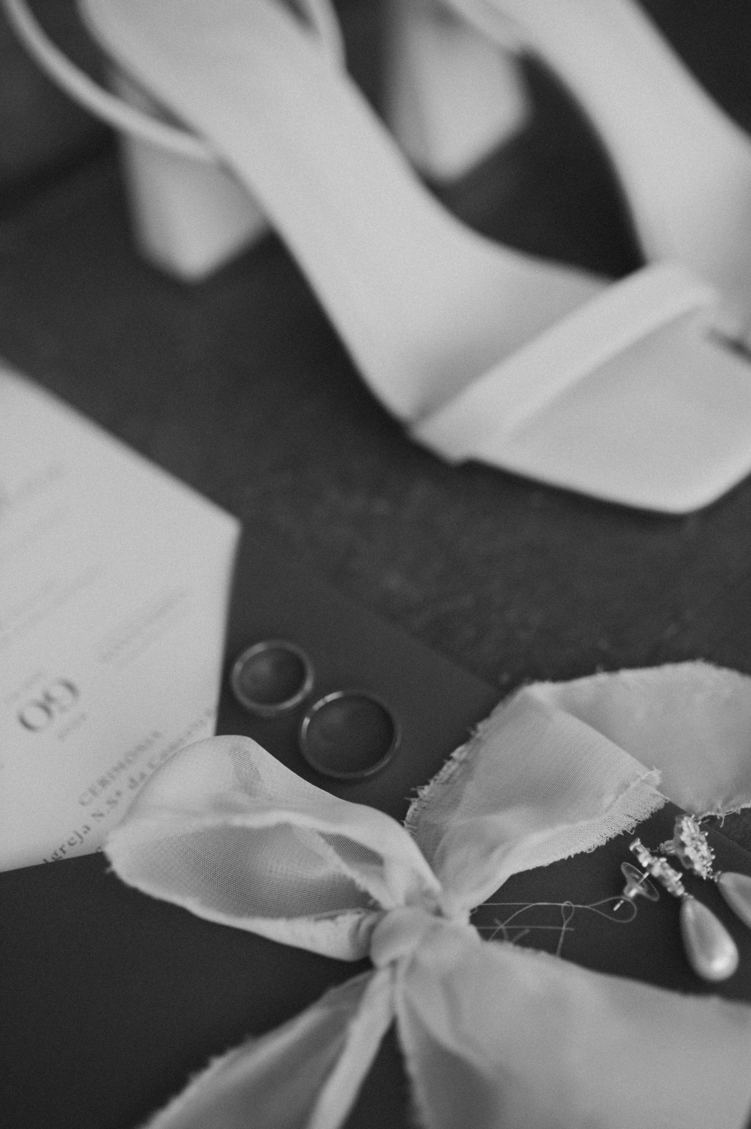 Wedding details including white shoes, rings and a ribbon laid out on dark surface.