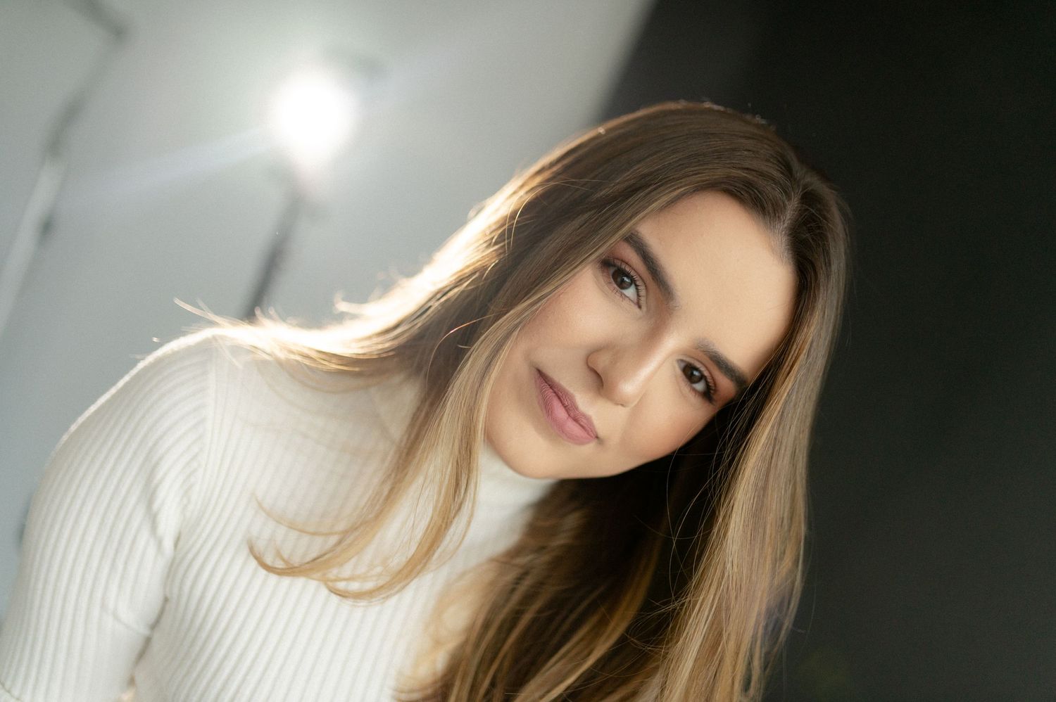 Portrait of a person in a white turtleneck sweater captured in soft lighting.