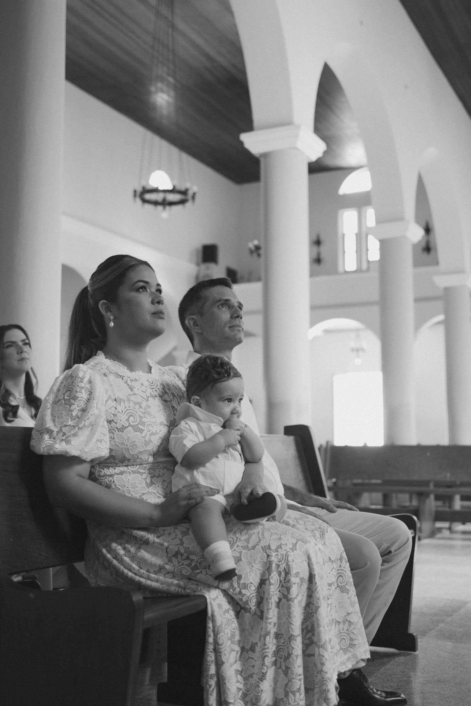 A group sits together in a church pew wearing formal white lace dresses during what appears to be a service.
