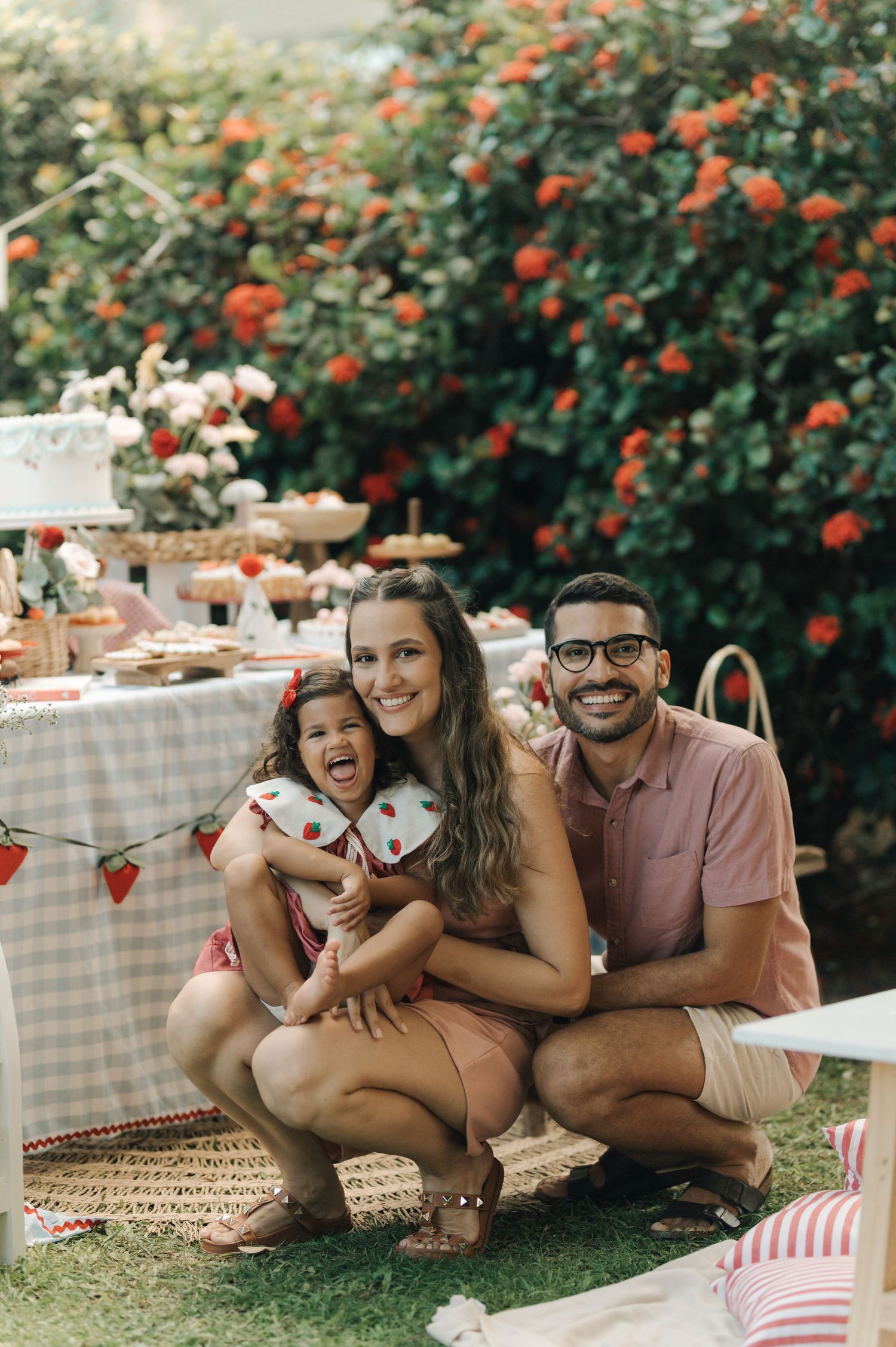 A festive outdoor picnic scene with red flowers and a decorated table in the background.