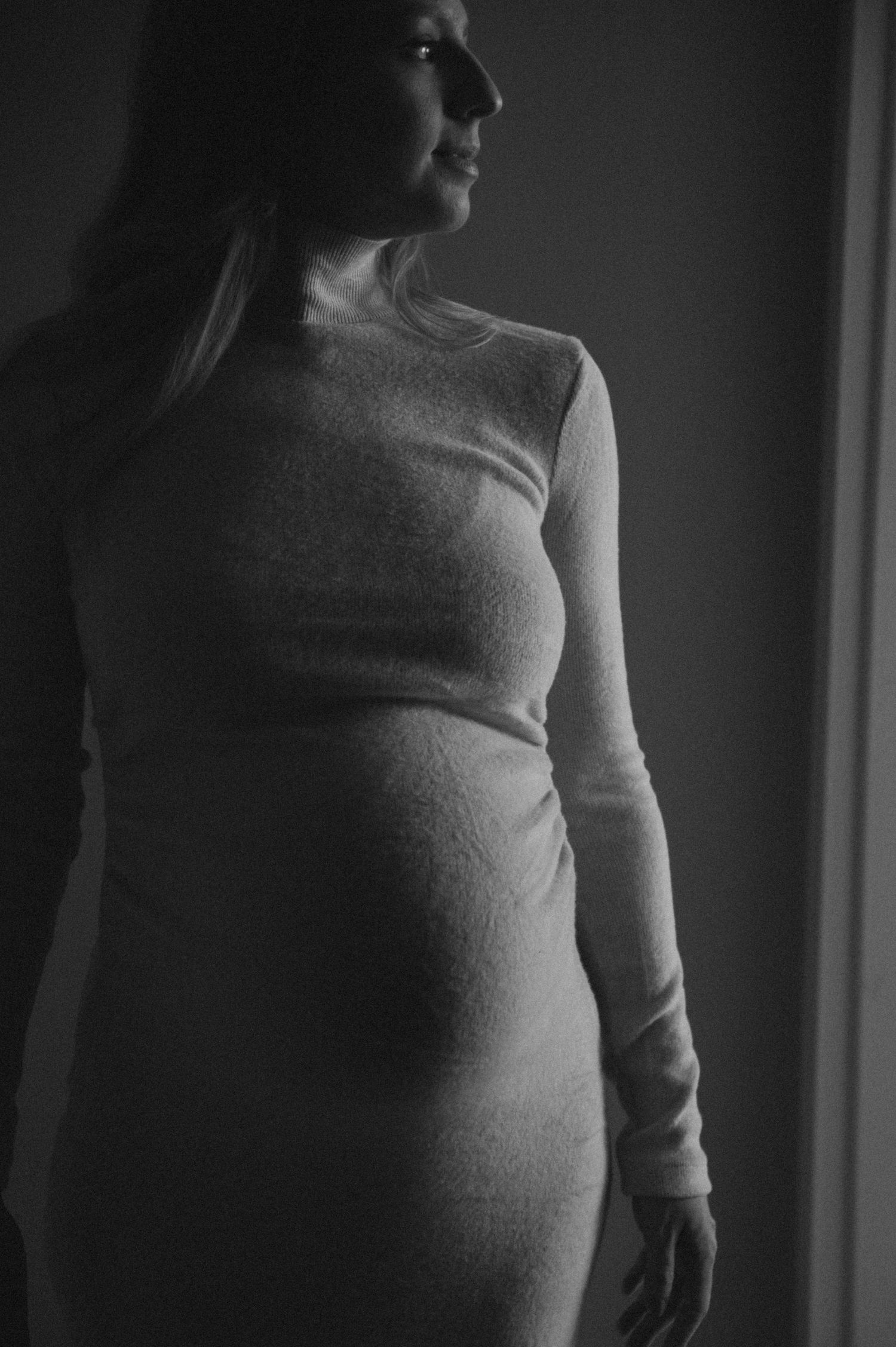 Dramatic side profile maternity portrait in monochrome lighting emphasizes elegant form.