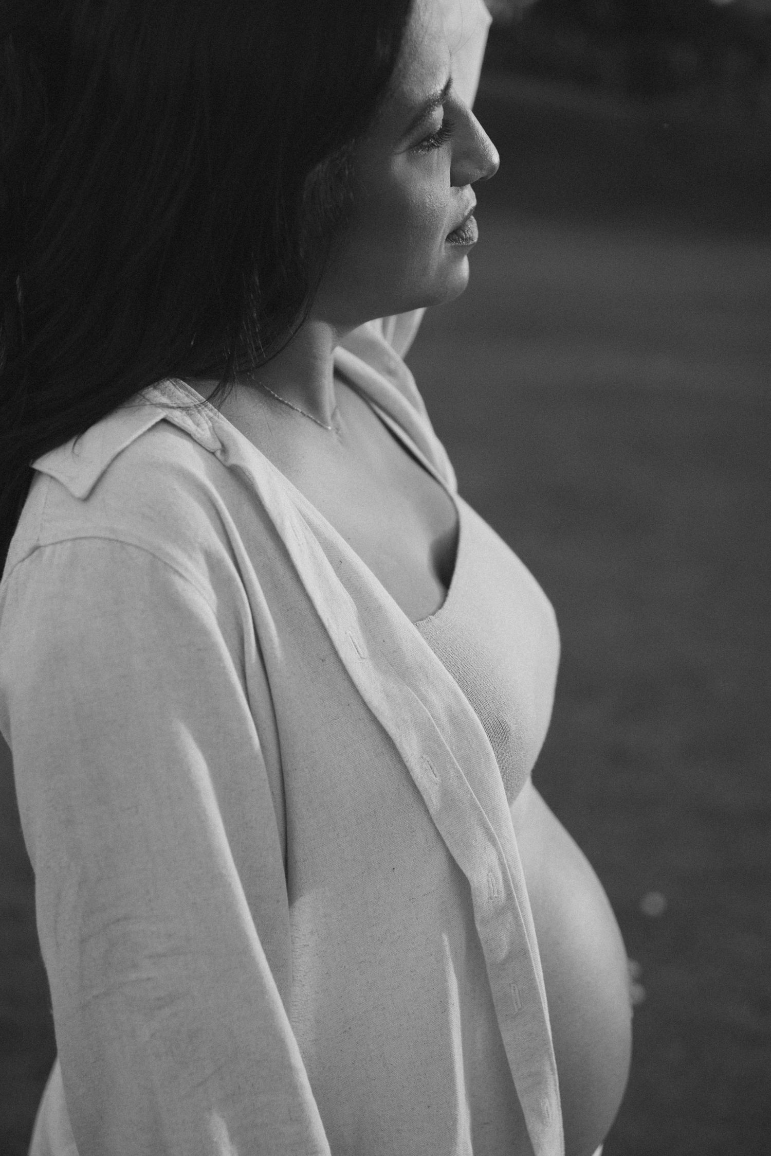 Profile maternity portrait in black and white showing pregnant silhouette in white clothing.