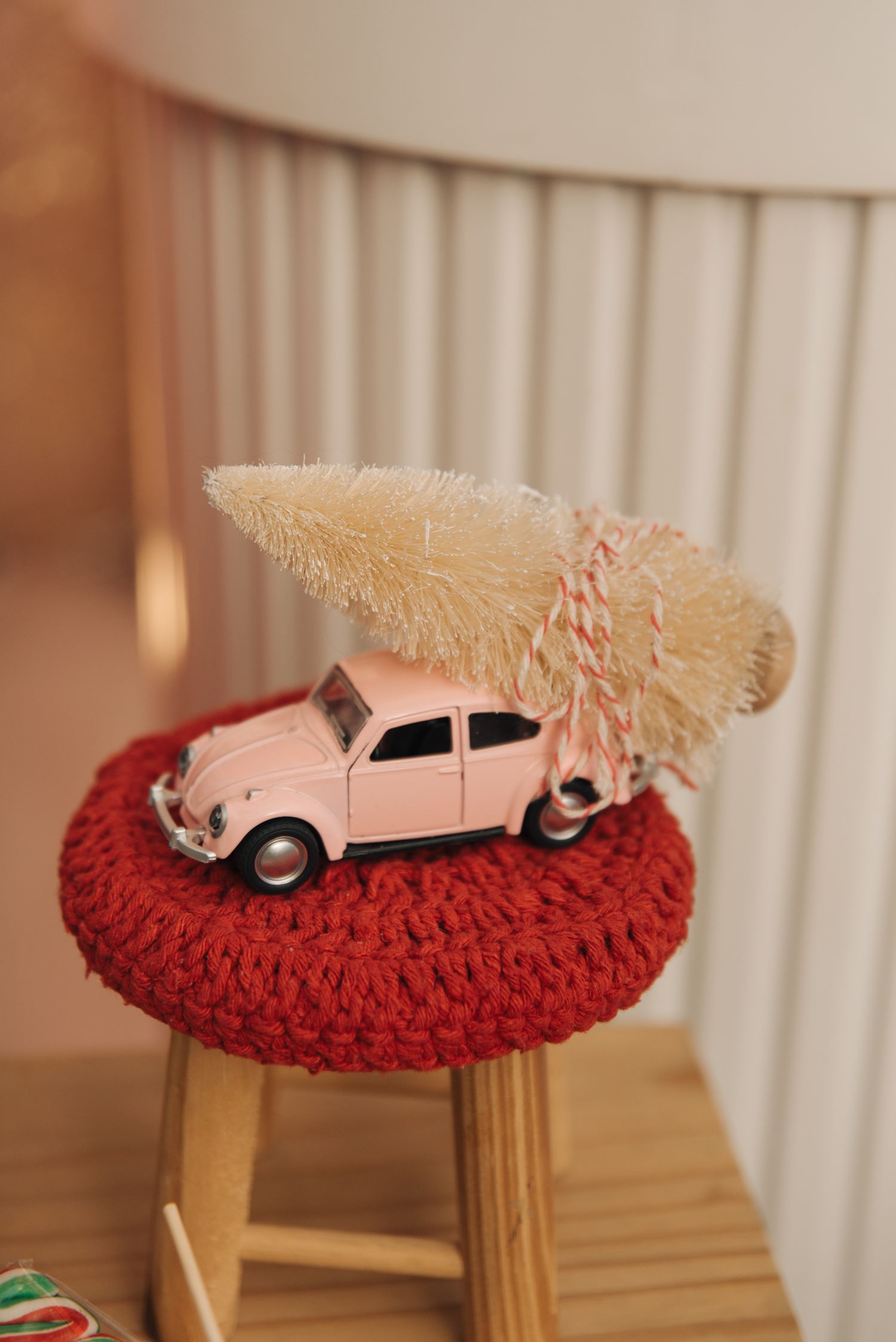 Pink toy car carrying miniature Christmas tree on red crocheted stool cover.