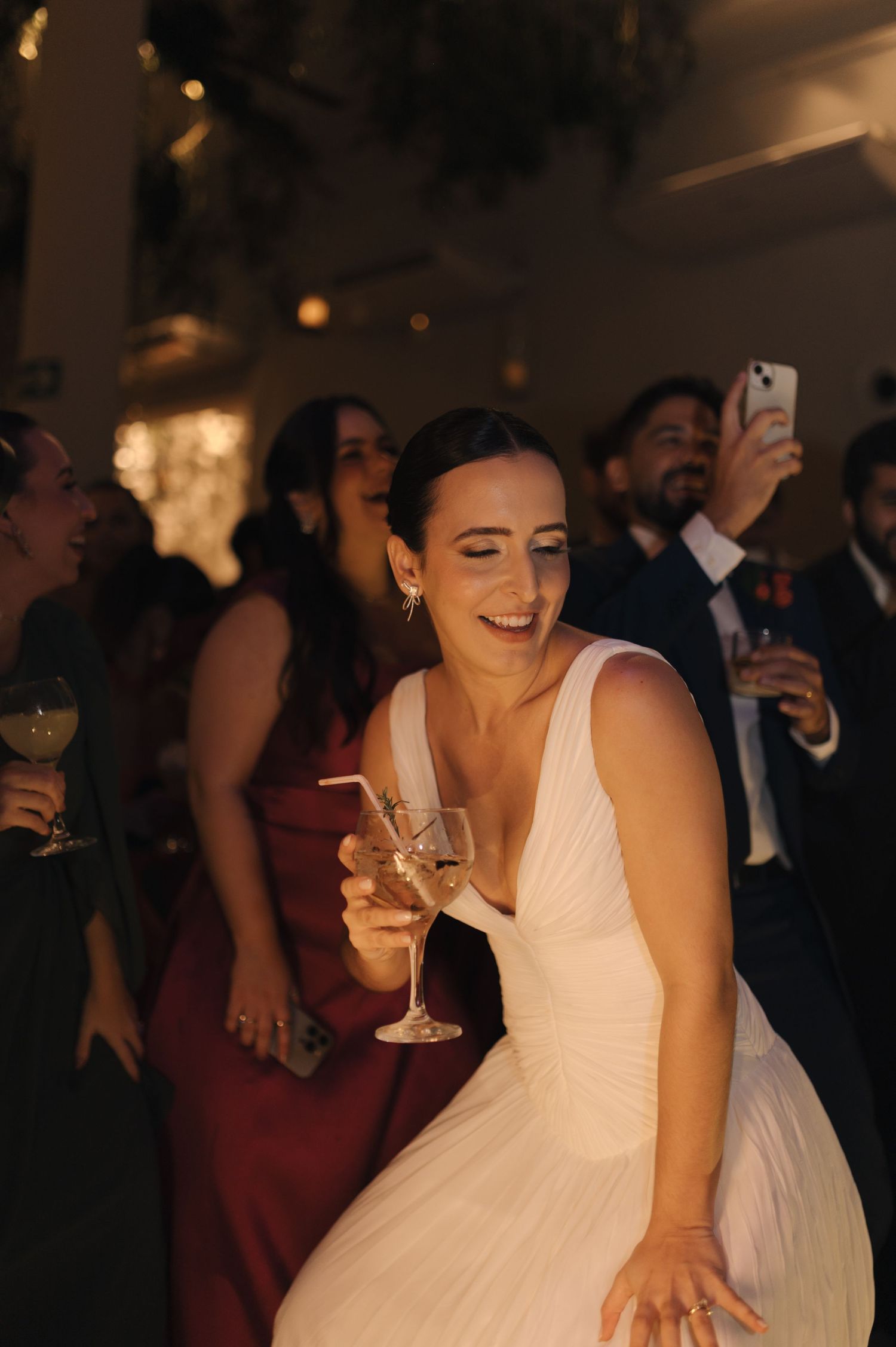 Wedding guests dance and celebrate on a dimly lit dance floor at an evening reception.
