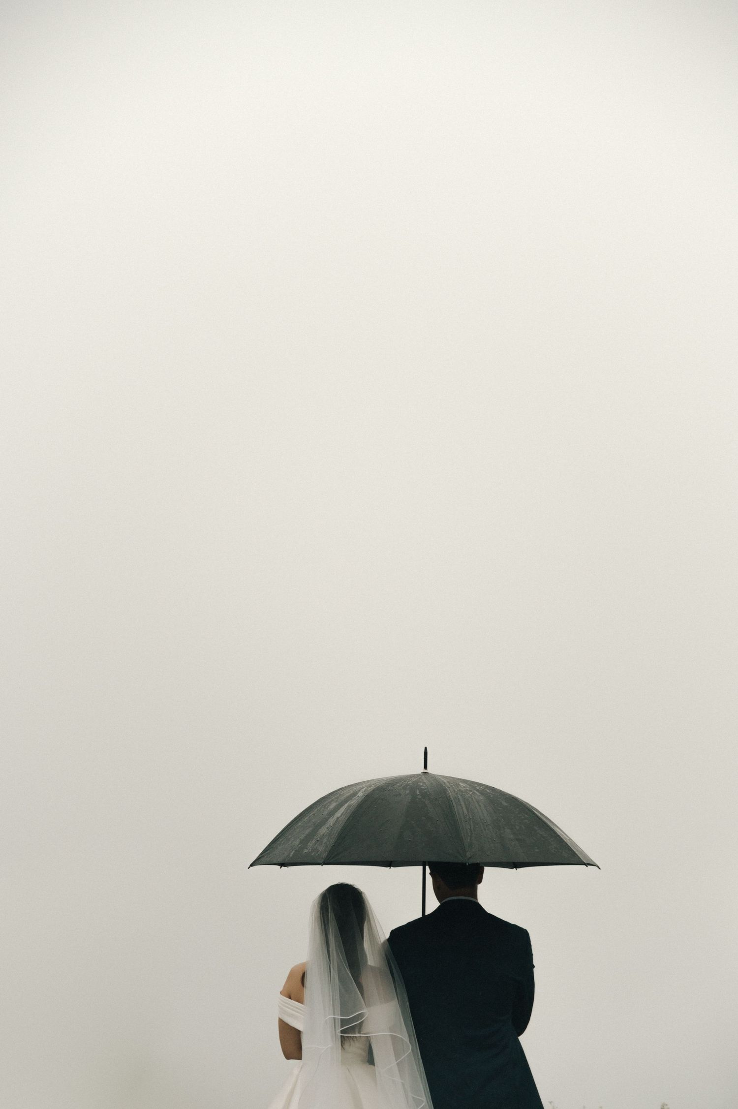Artistic black and white wedding photo featuring a couple sharing an umbrella in a minimalist setting.