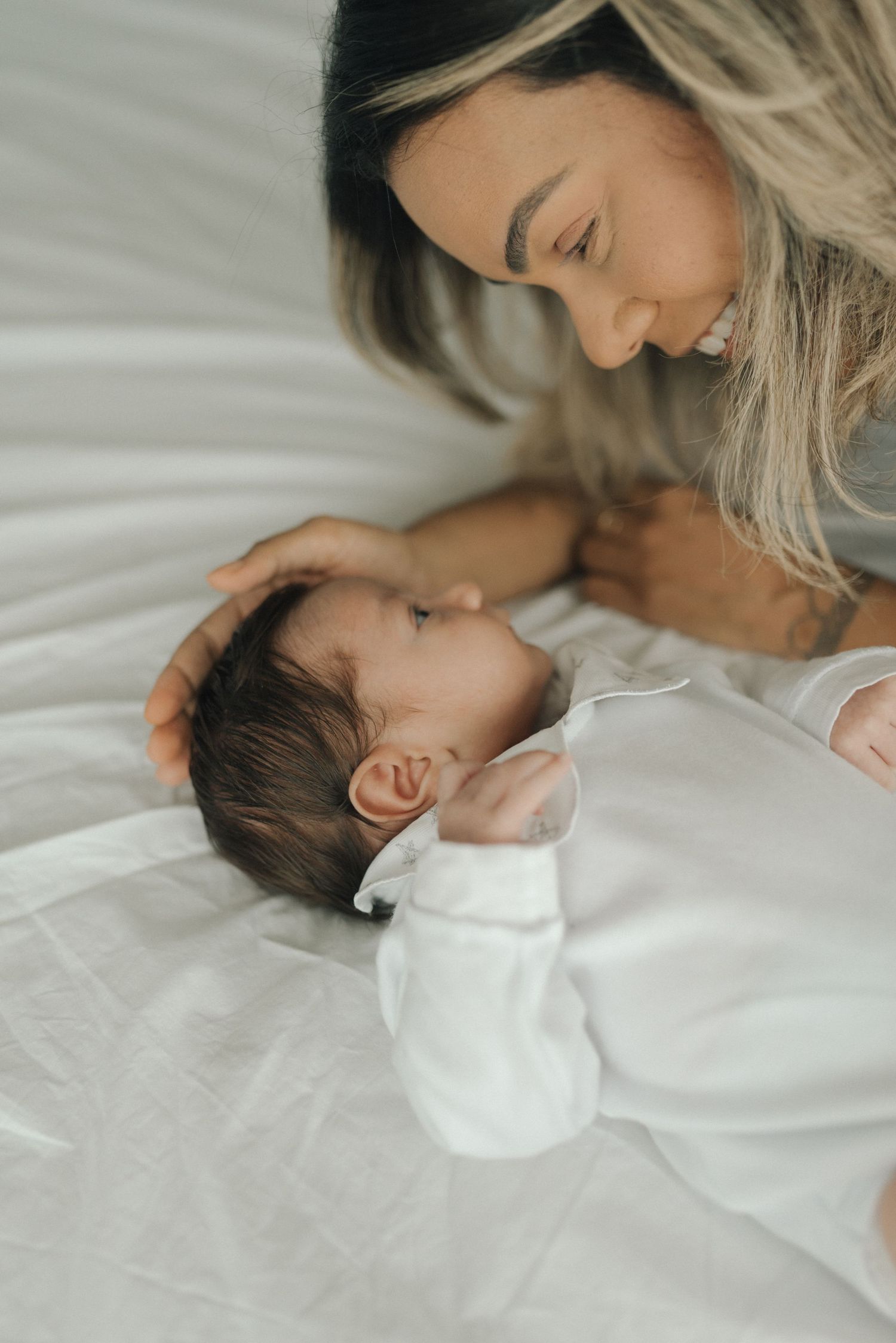 A tender moment between mother and newborn baby lying on white bedding.