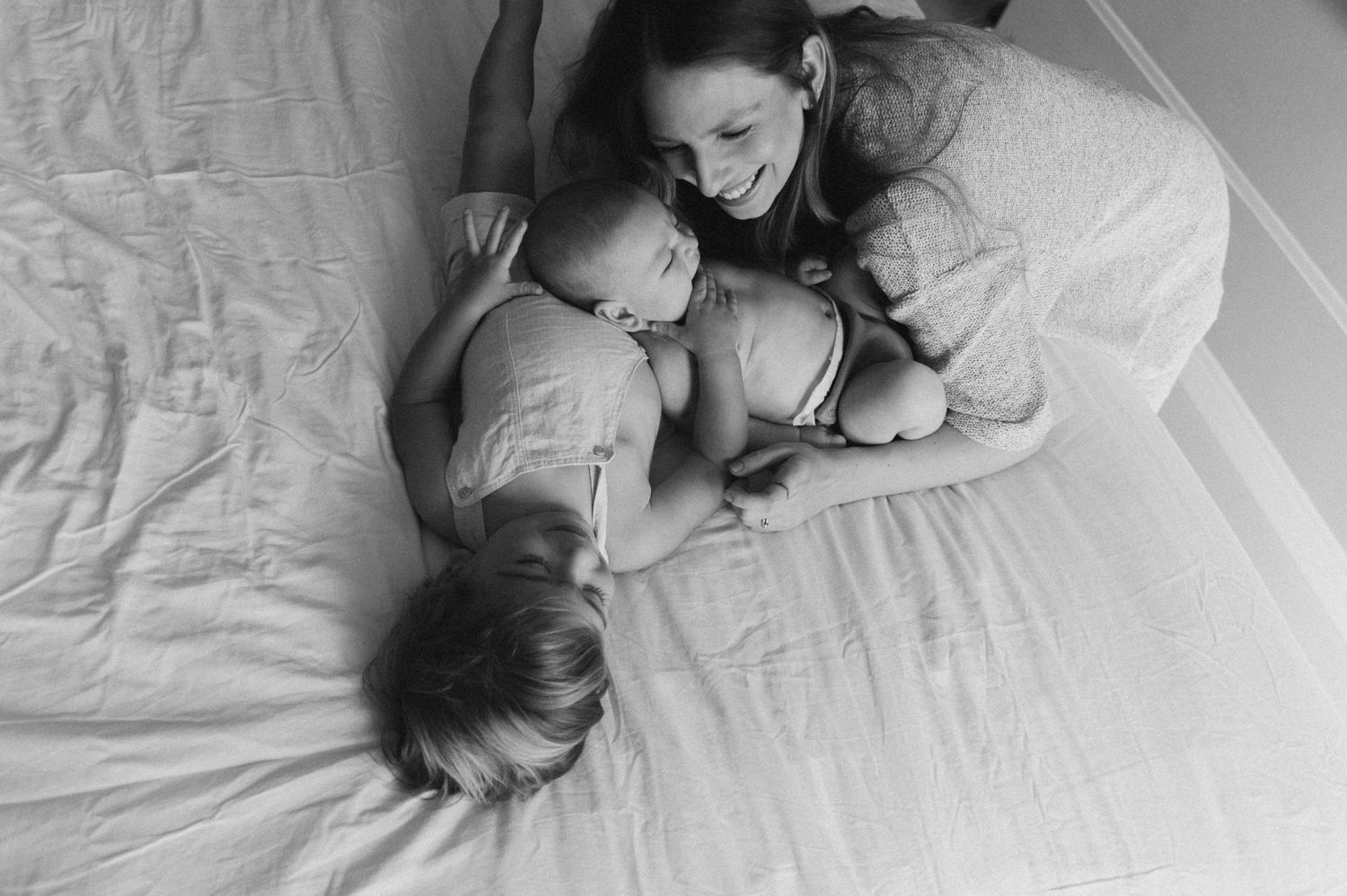 A series of black and white photographs showing tender moments between a parent and baby on white bedding.