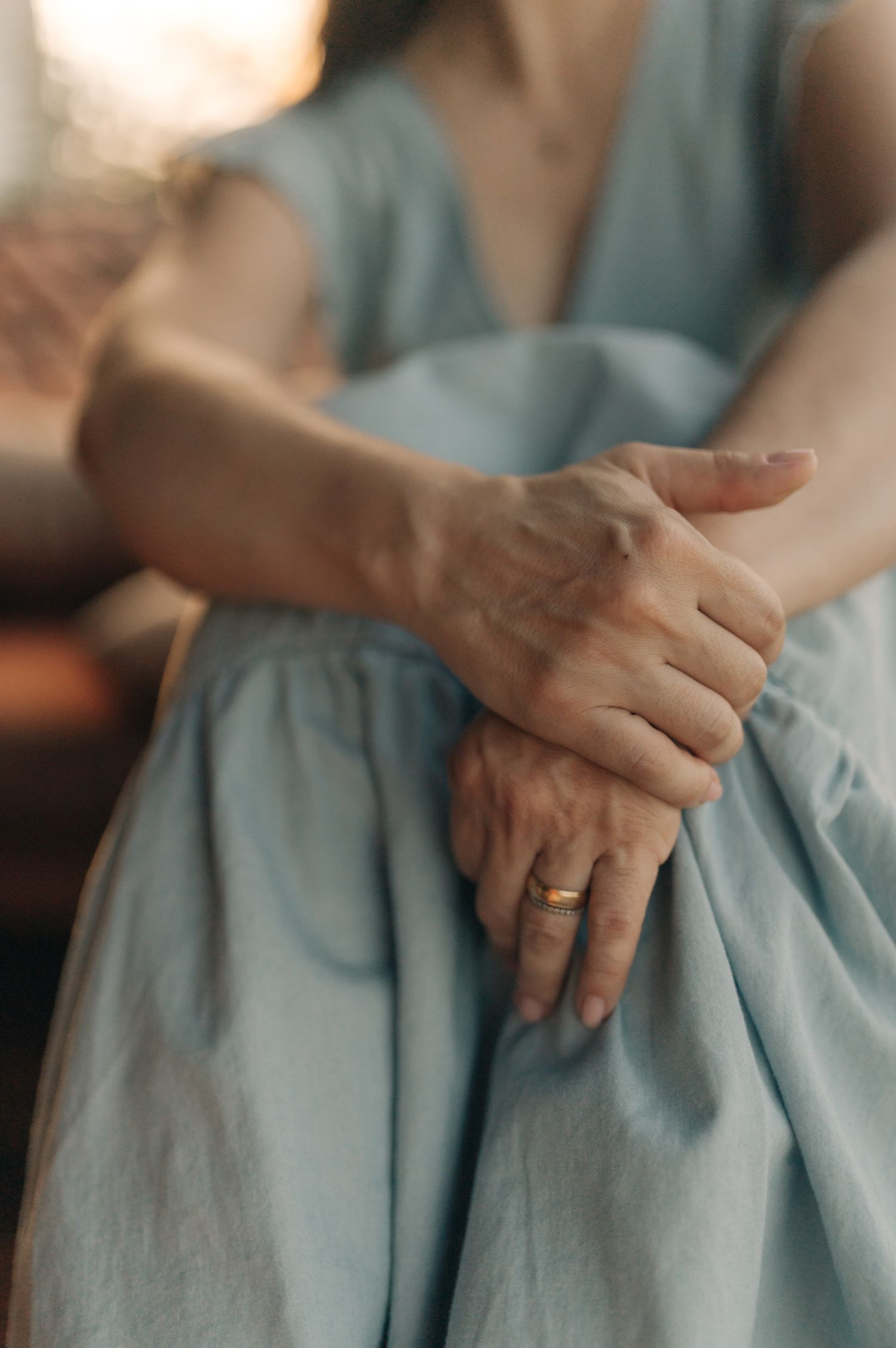 Close-up shot of hands resting on a light blue fabric dress, showing a ring.