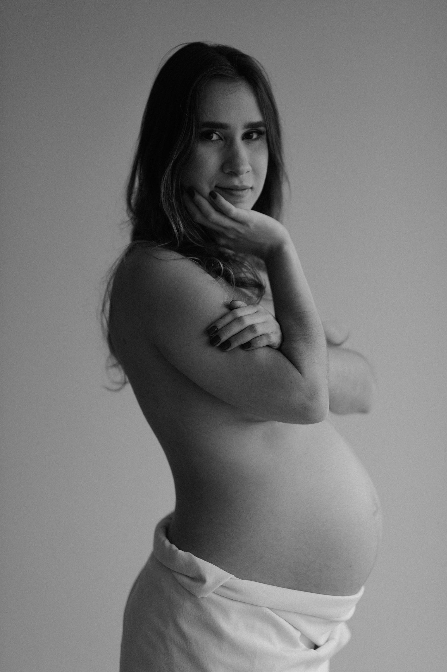 Black and white artistic maternity portrait showing profile pose against neutral background.