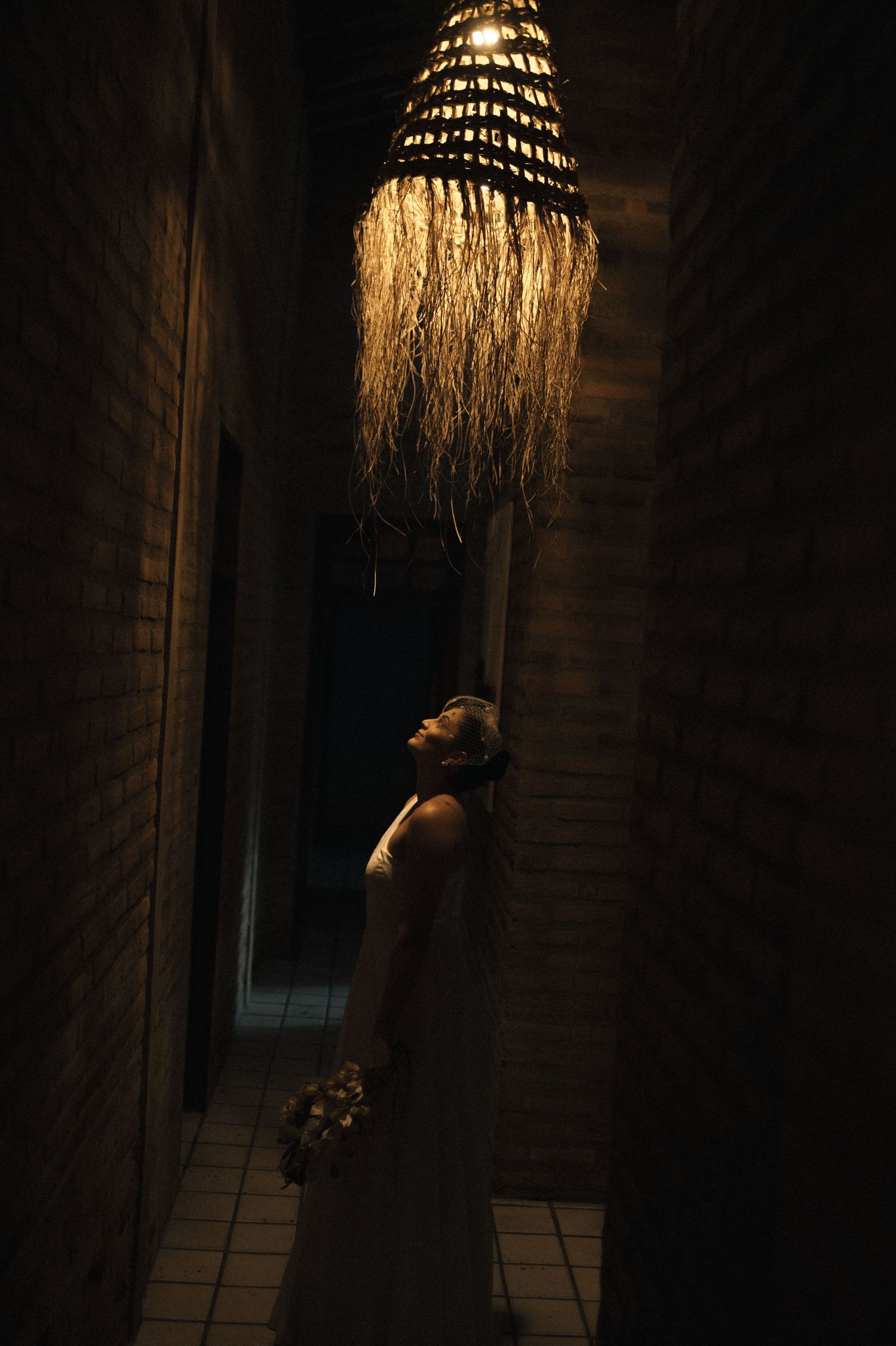 A dramatic silhouette stands beneath an illuminated chandelier in a dark room creating a moody atmosphere.