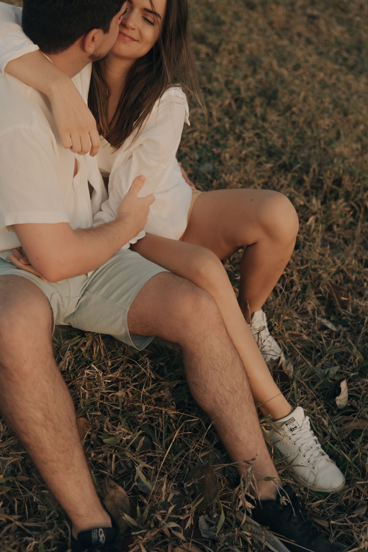 Intimate couple in white clothes sharing tender moment on dry grass.